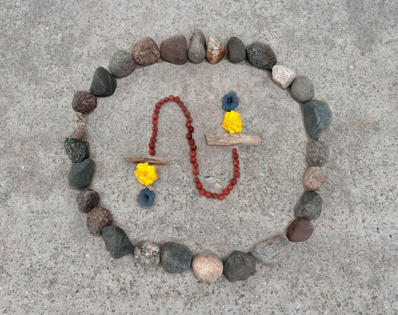 Nature mandala: a circle of stones with a red bead necklace, driftwood and yellow and blue flowers