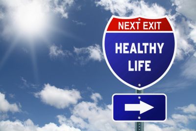 Illustrated highway sign reading Next Exit Healthy Life with a directional arrow against a sunny sky