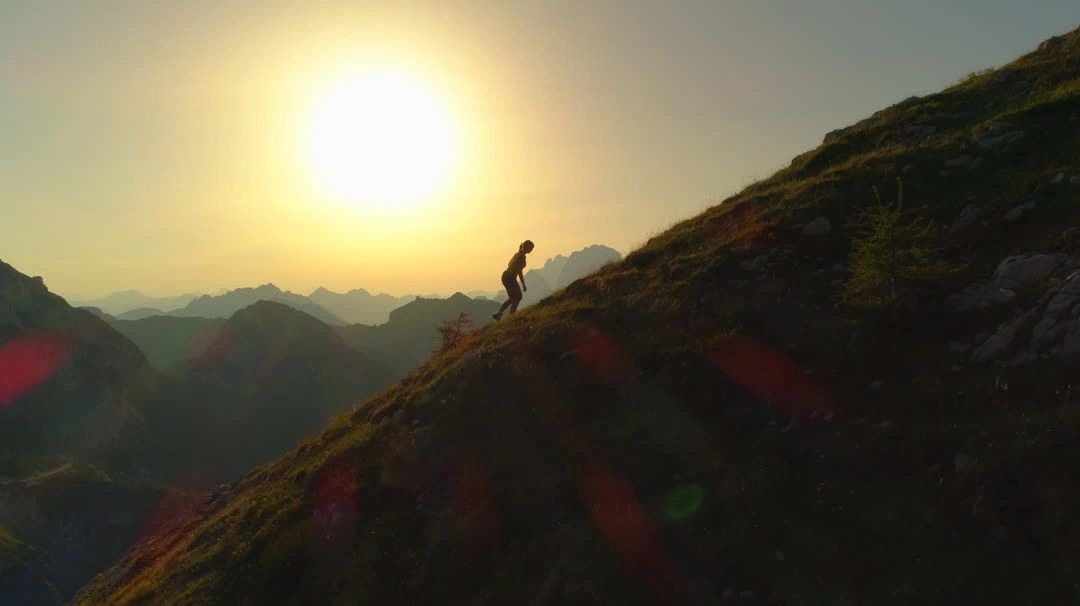 Silhouette of a person climbing a steep mountain slope at golden-hour sunset