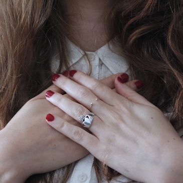 Close-up of a woman's hands with red nails and a silver ring crossed over her heart