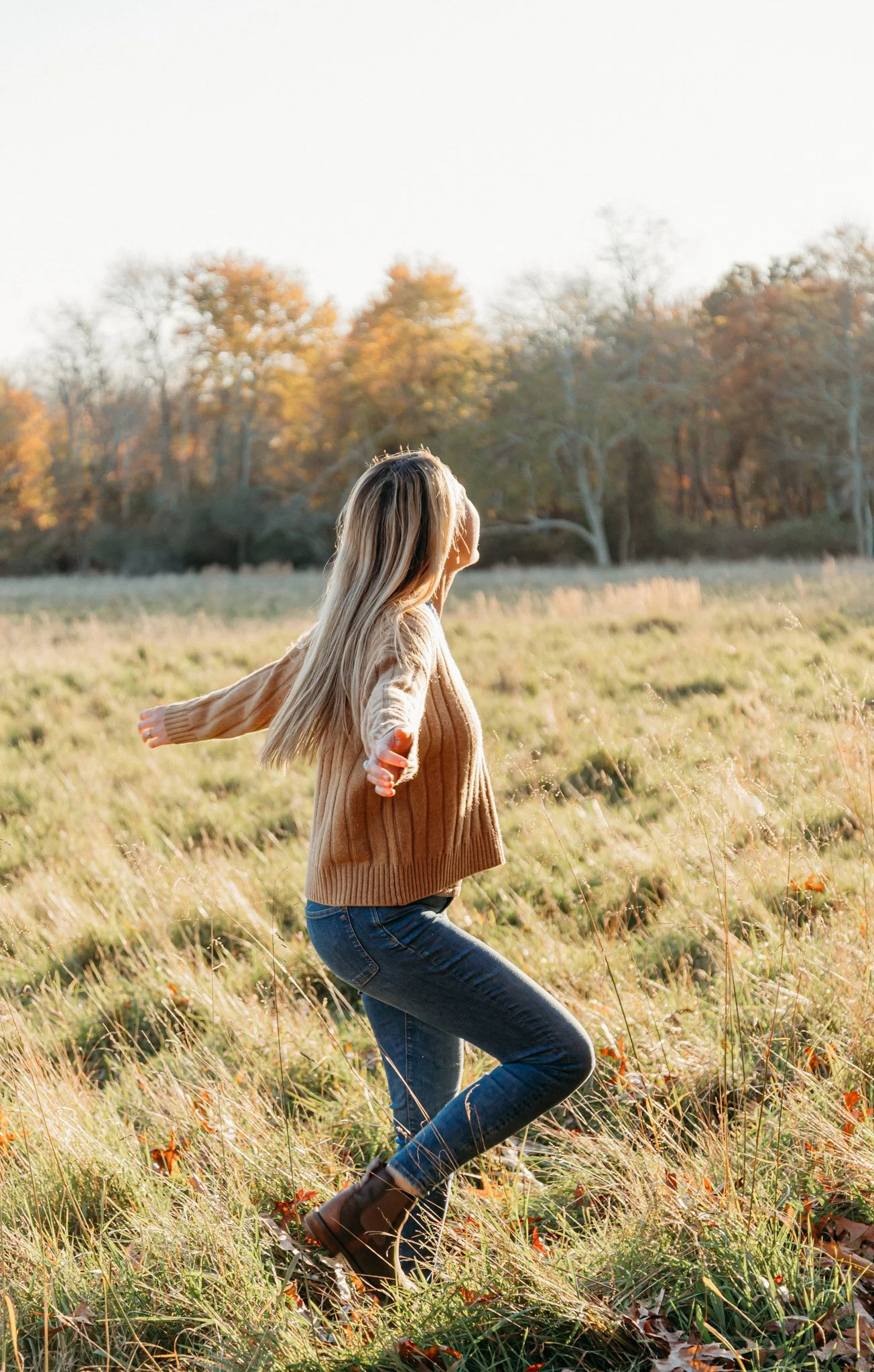Hannah dancing and twirling in an autumn meadow with arms outstretched.