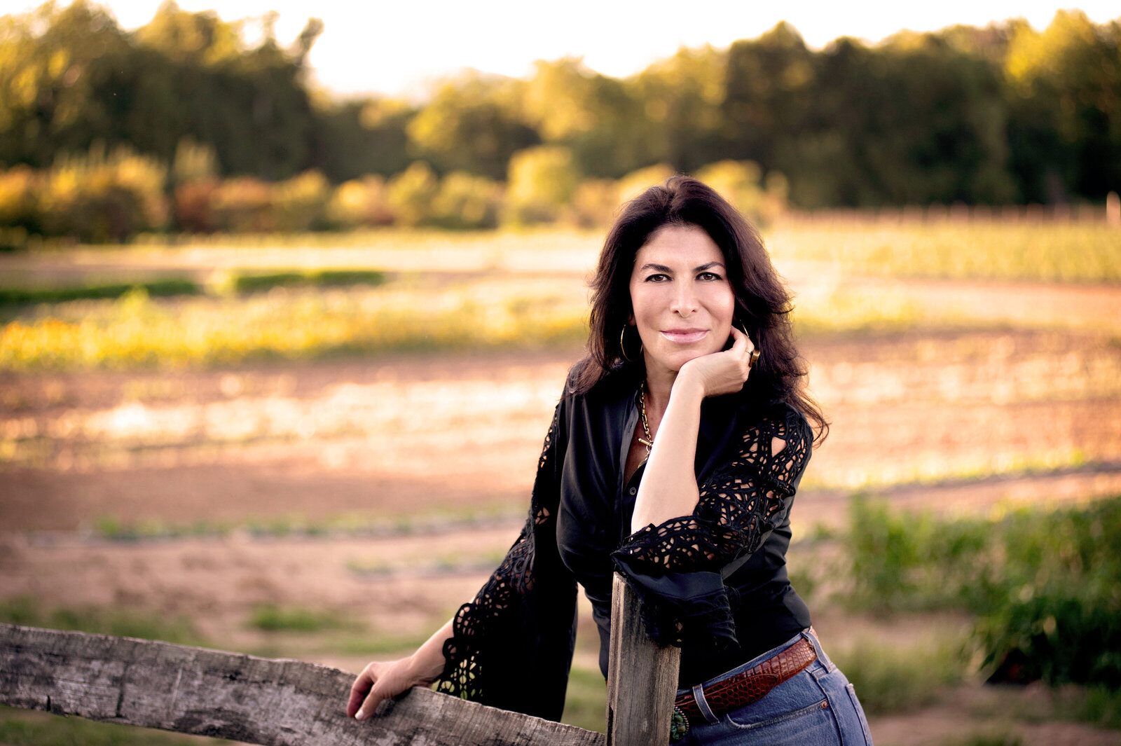 Lisa Cypers Kamen leaning on a wooden fence in a golden-hour farm field