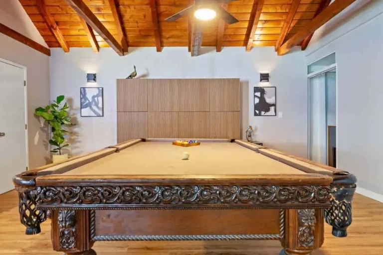 Billiards and game room with an ornate carved pool table under wood beams