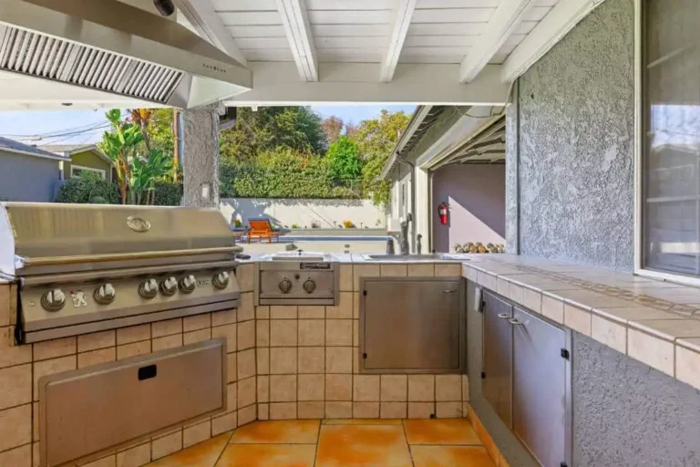 Outdoor covered kitchen and BBQ area with a stainless steel grill and pool behind