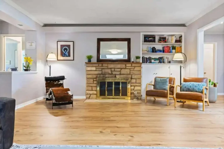 Living room with stone fireplace, leather lounge chair and built-in bookcase, wider angle