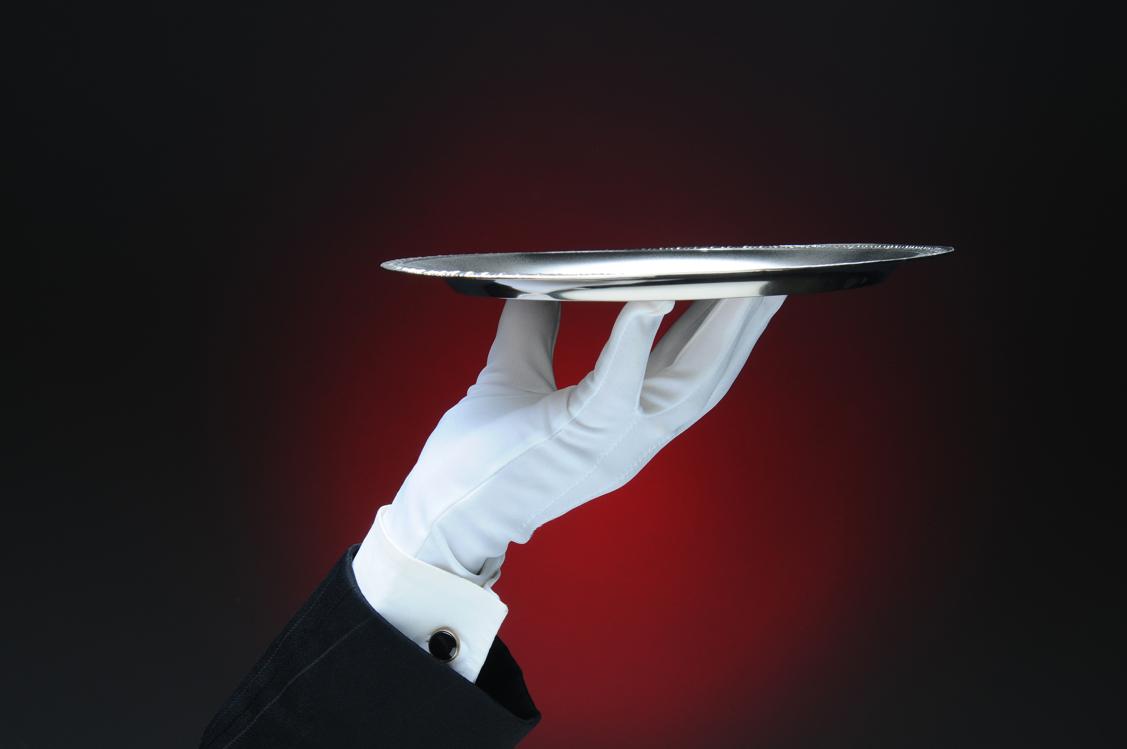 Gloved butler's hand holding a silver serving tray against a dark red background