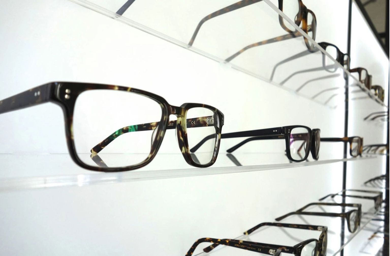 Eyeglass frames displayed on clear acrylic wall-mounted shelves at HMY Vision