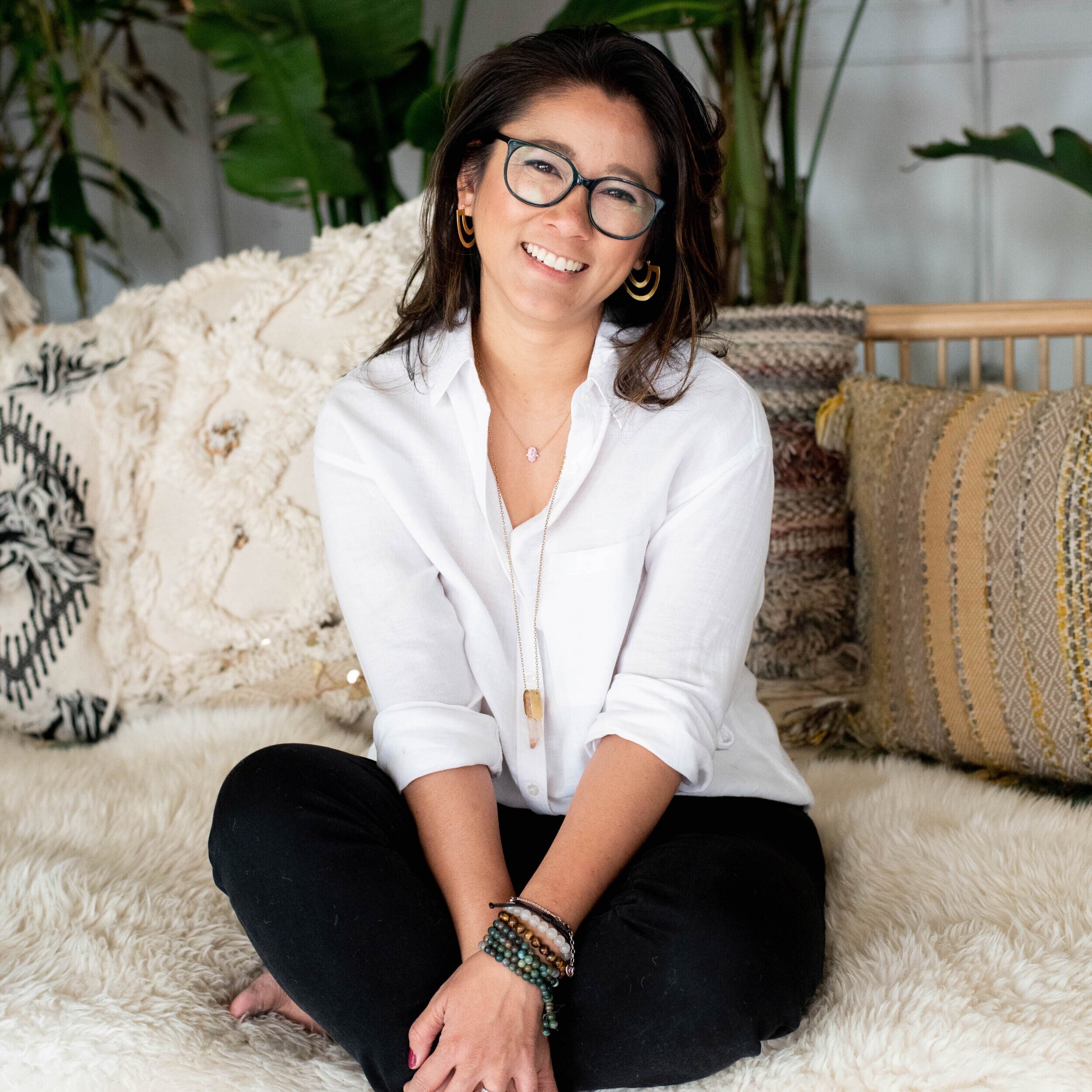 Mimi Truong, woman with glasses seated cross-legged among bohemian pillows