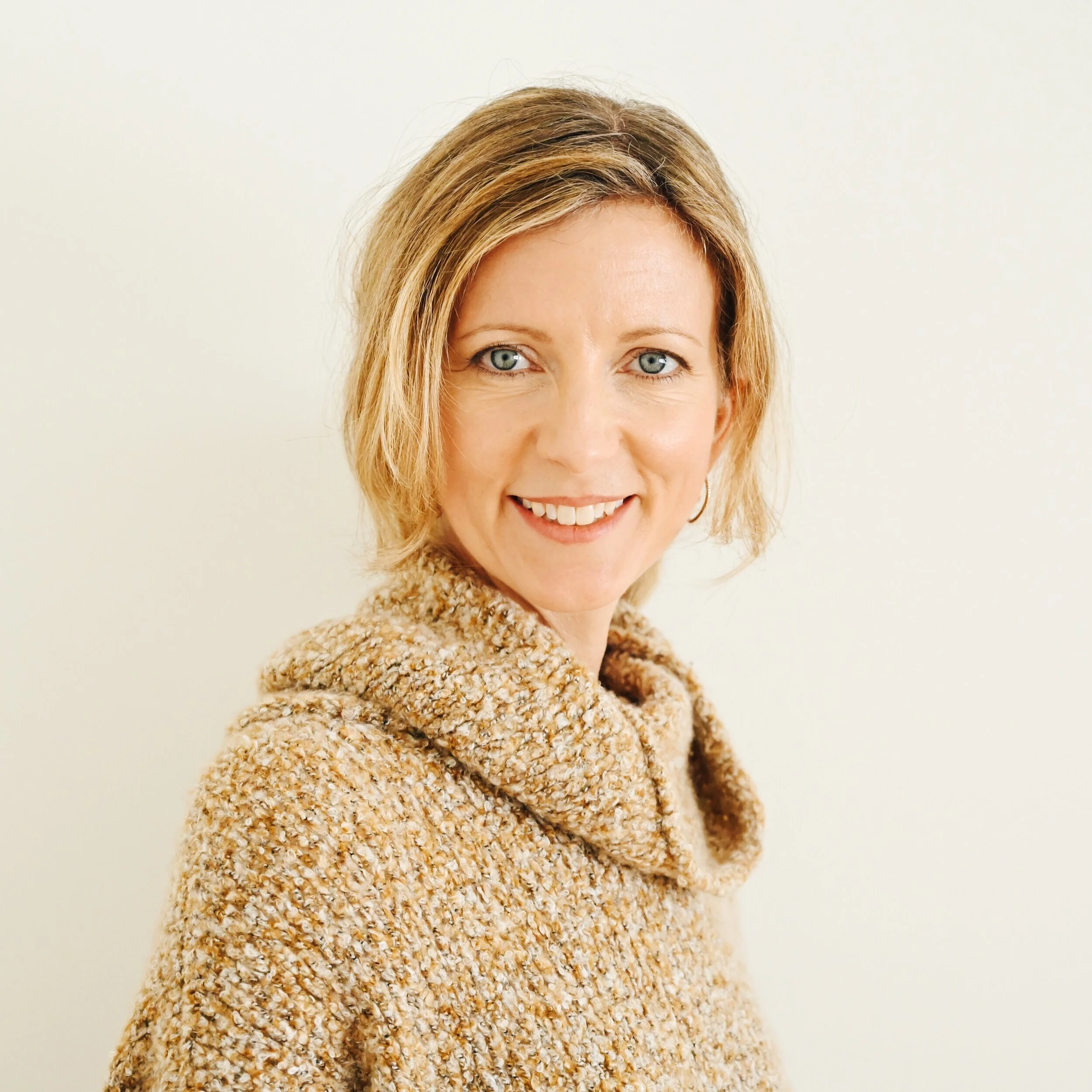 Danielle DeJoie, blonde woman in a tan knit wrap sweater