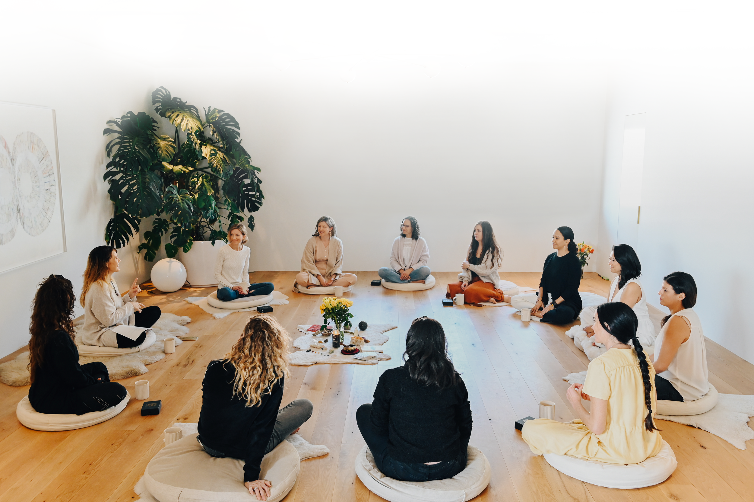 A circle of women seated on cushions in a bright studio during a hōm gathering