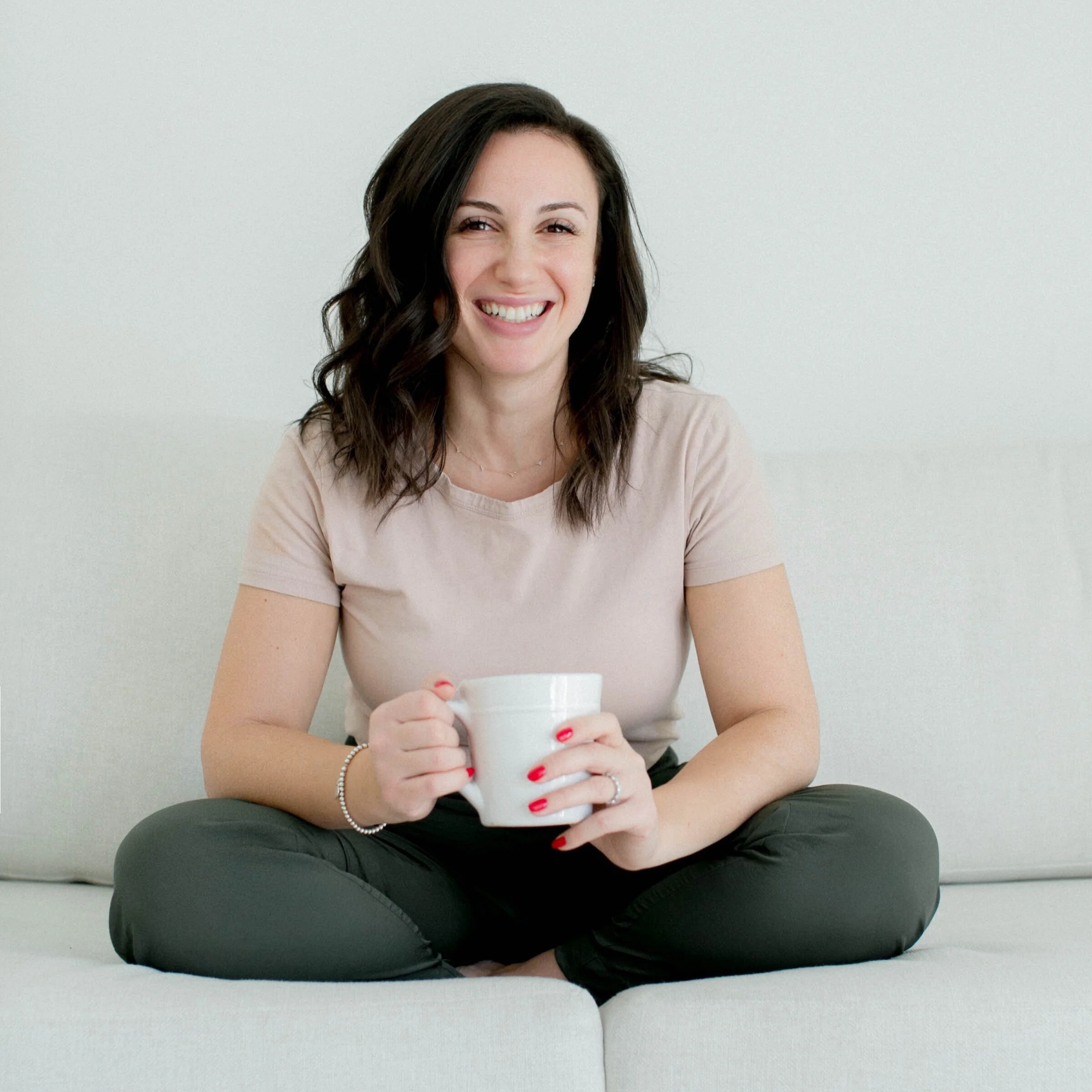 Dr. Jane Shomof seated on a couch holding a white mug