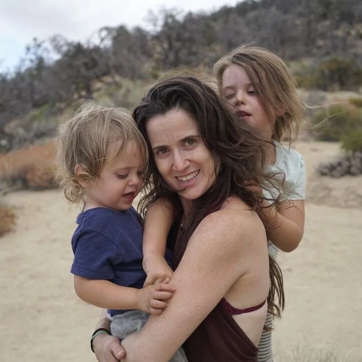 Hagar Harpak smiling outdoors while holding two young children