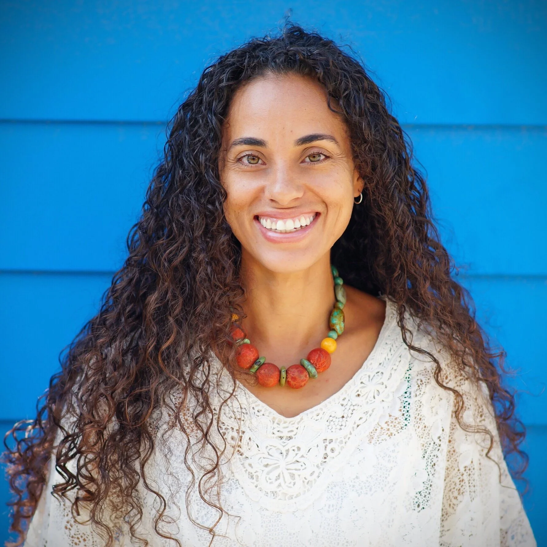 Nicole LaCour-Wordlaw with curly hair and a beaded necklace against a blue wall