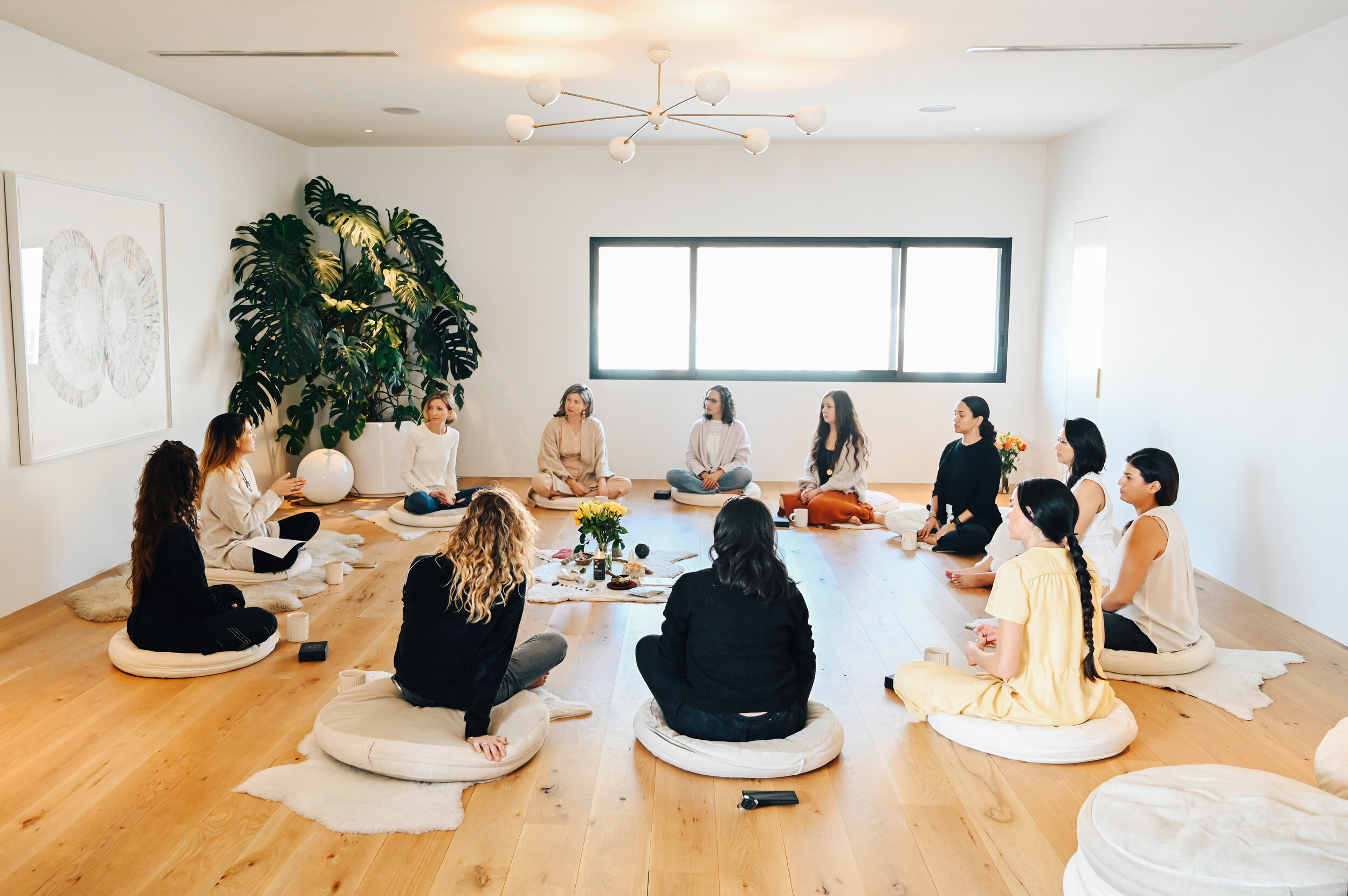 Women seated in a circle on the hardwood floor of a light-filled studio
