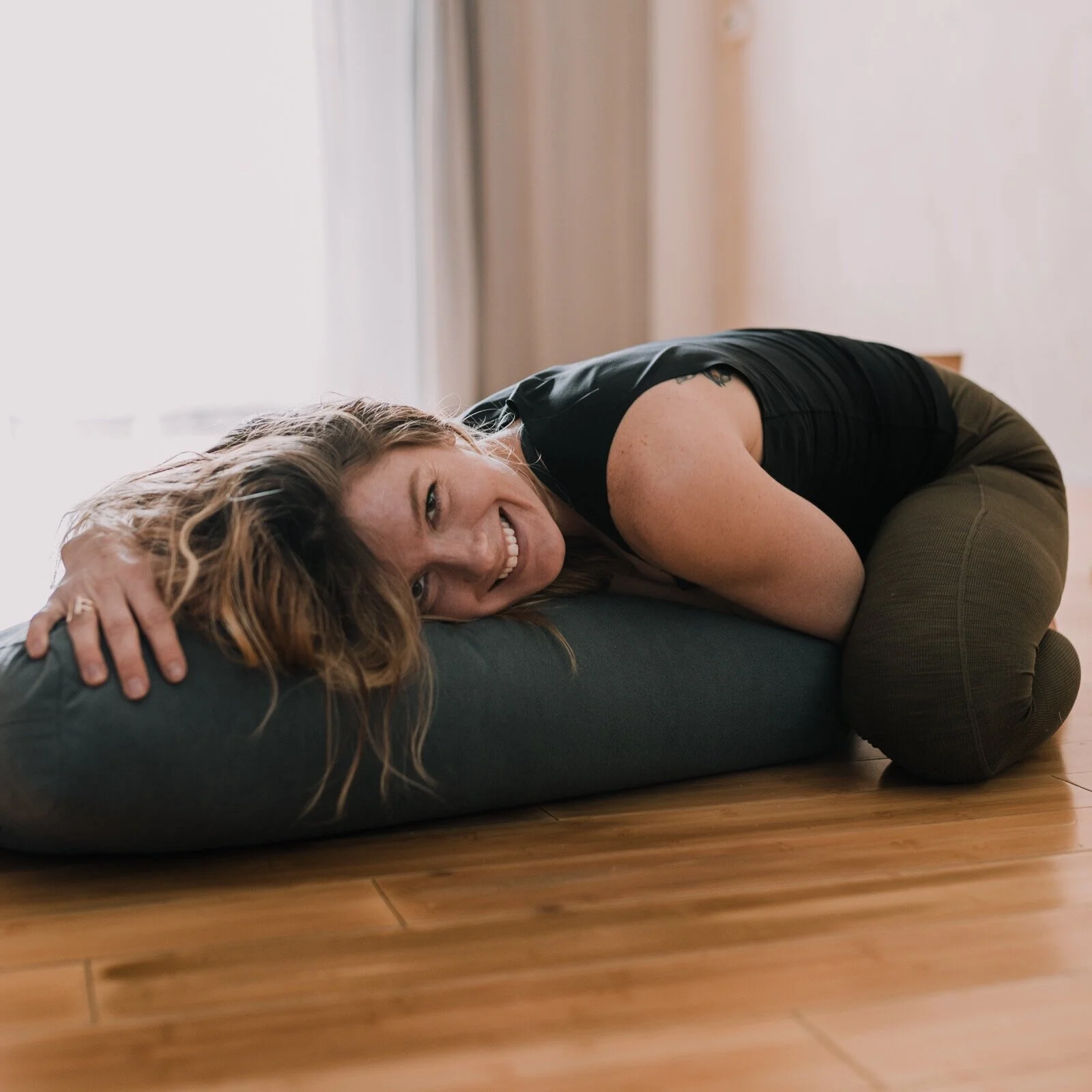 Leia Hays in black workout clothes resting on a yoga bolster