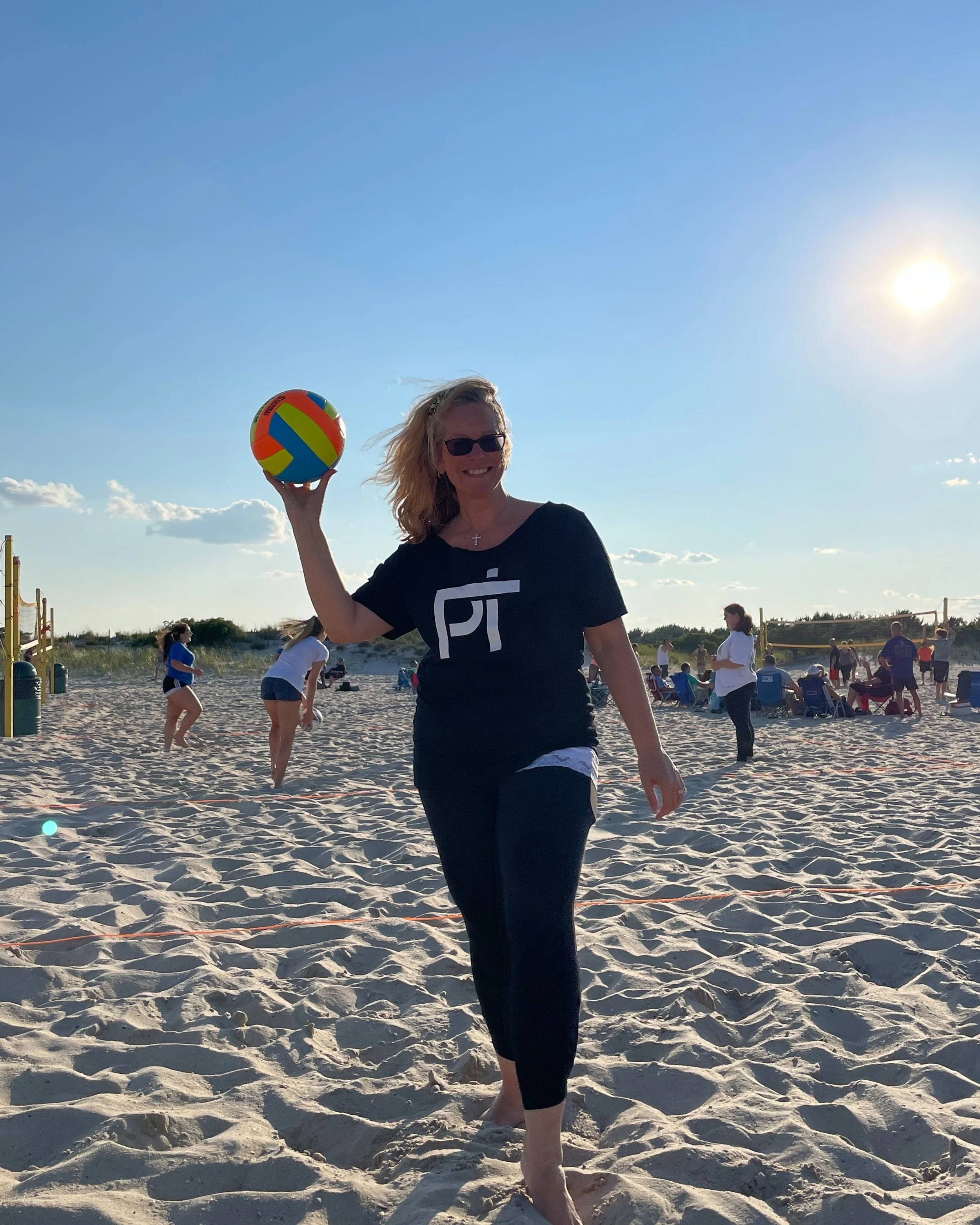 Dawn Johnstone in a black House of Physical Therapy shirt holding a volleyball on the beach