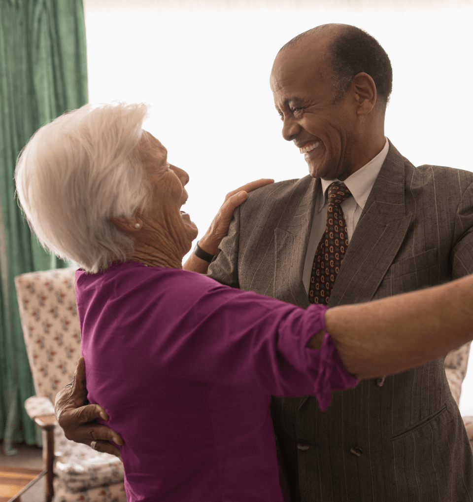 A happy senior couple dancing together and smiling at each other indoors
