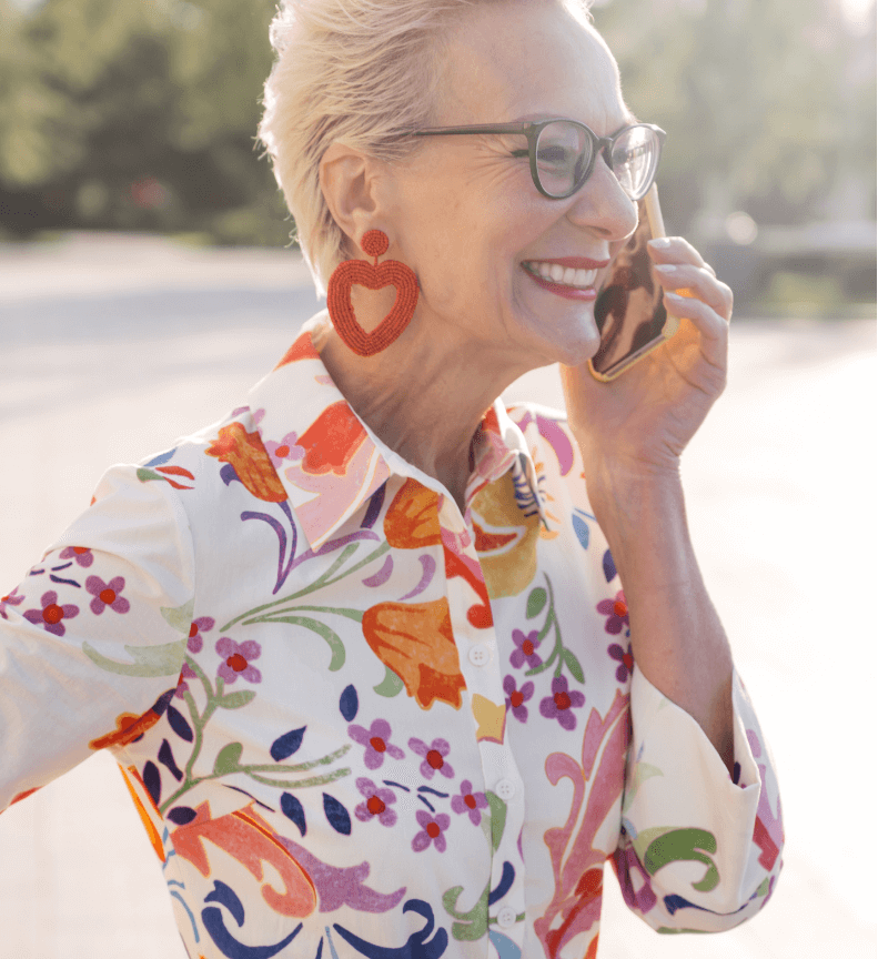 A stylish older woman with white hair and glasses laughing while talking on the phone outdoors