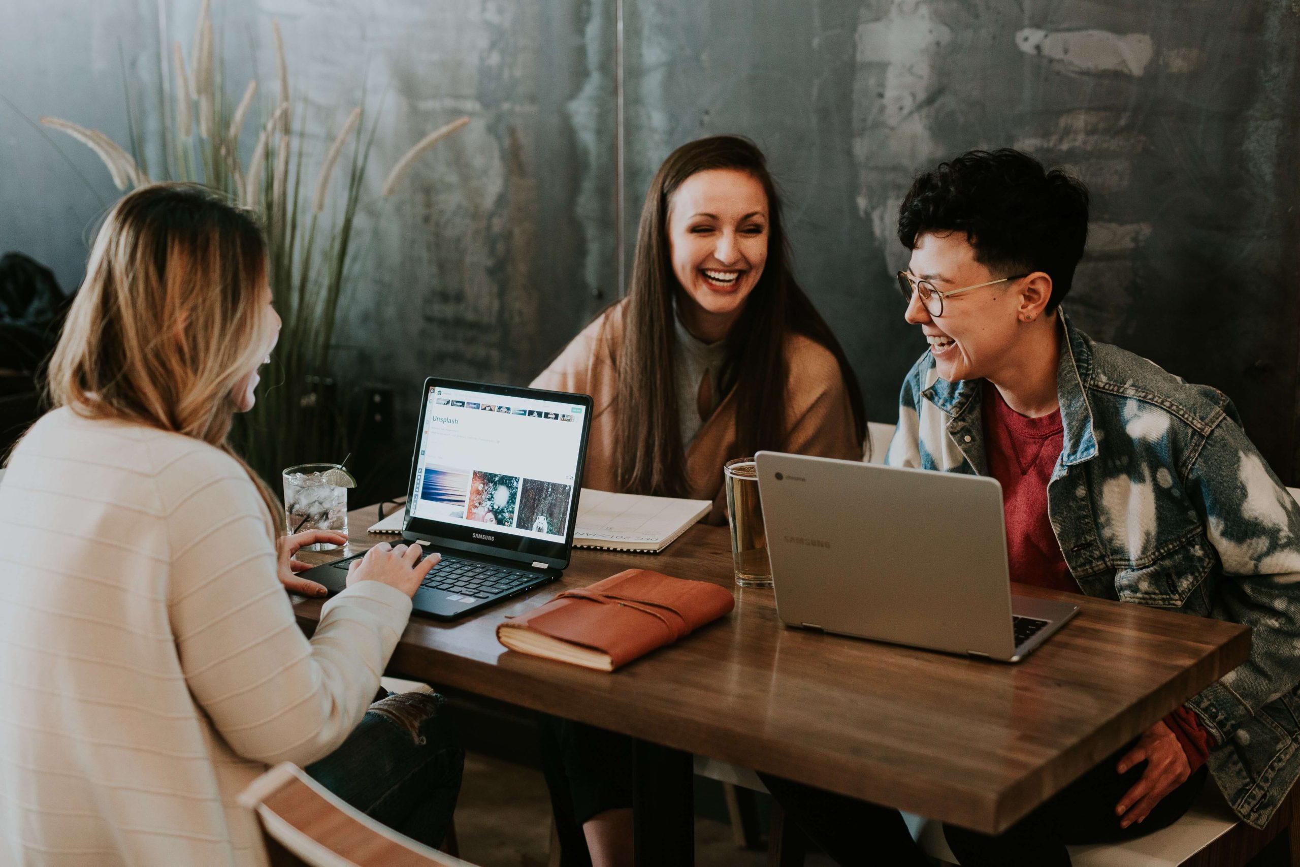 Three young professionals laughing and collaborating around a table with laptops