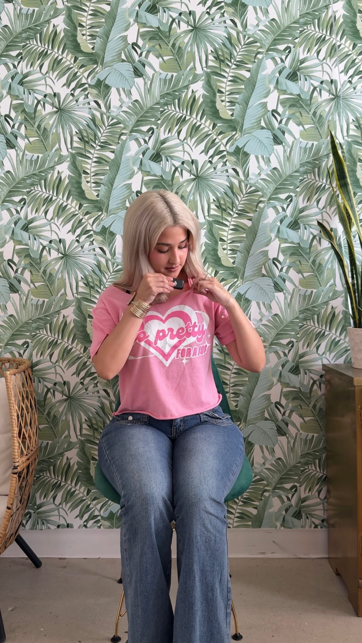 Team member in a pink graphic t-shirt seated in front of the tropical leaf wallpaper