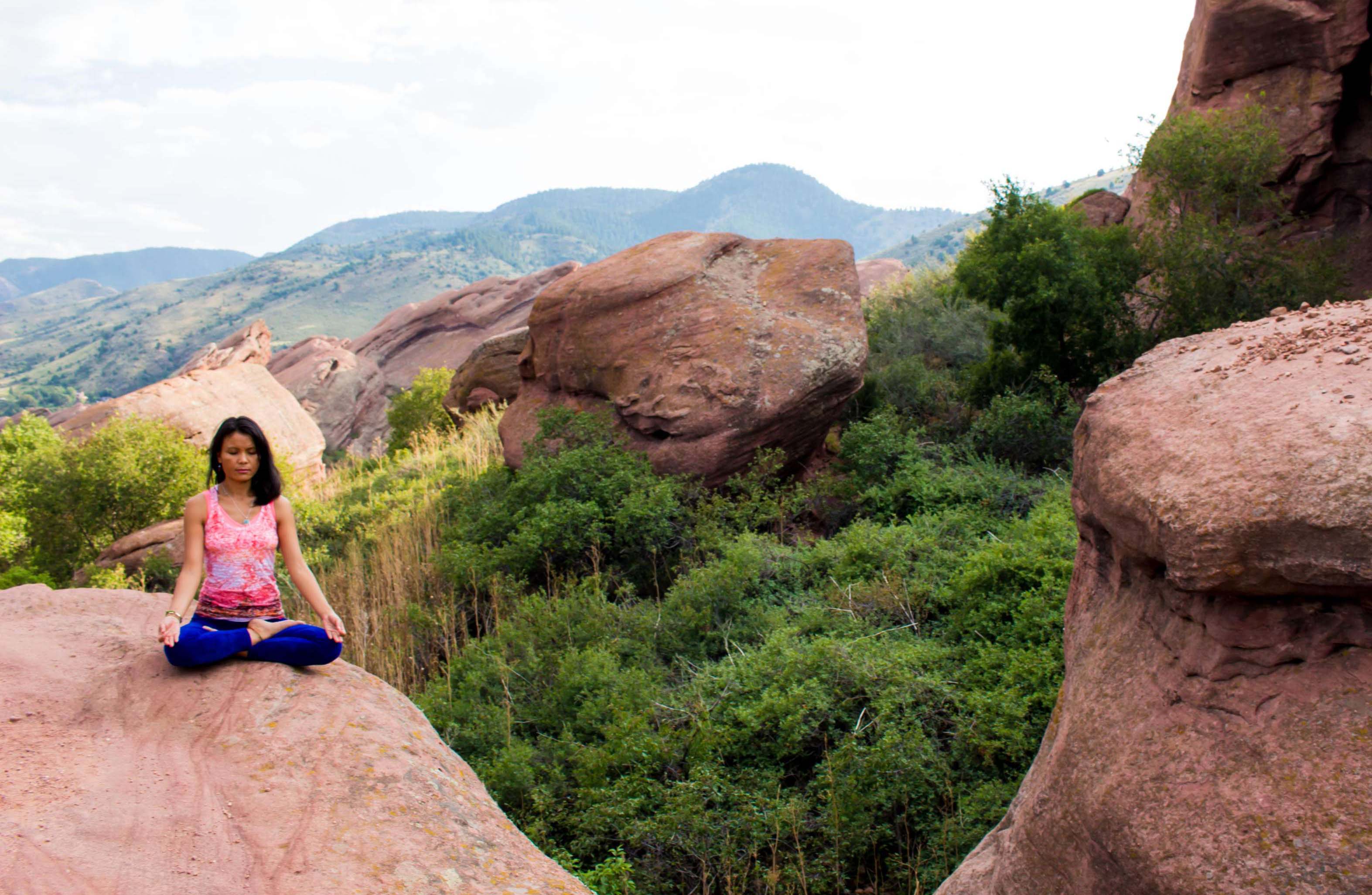 Penpa Dolma seated in lotus meditation on the red rocks of Colorado with mountains behind