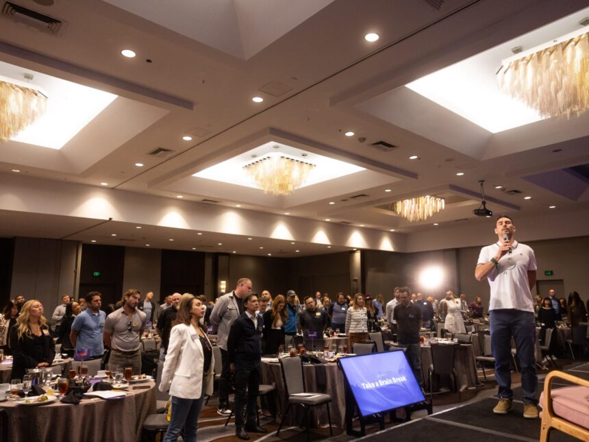 Presenter leading a large audience in a group wellness activity in a hotel ballroom