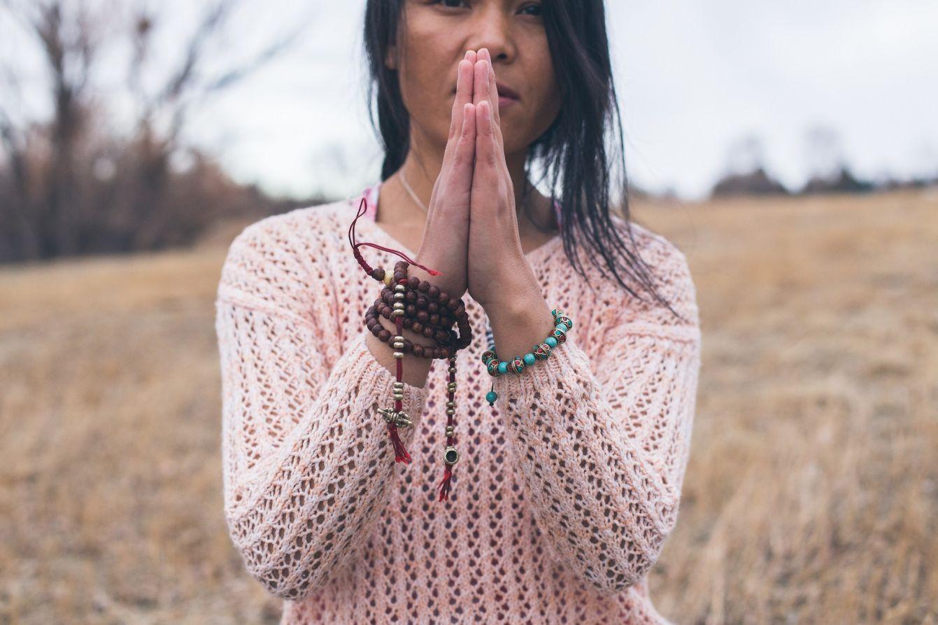 Close-up of prayer hands with mala beads in an outdoor field