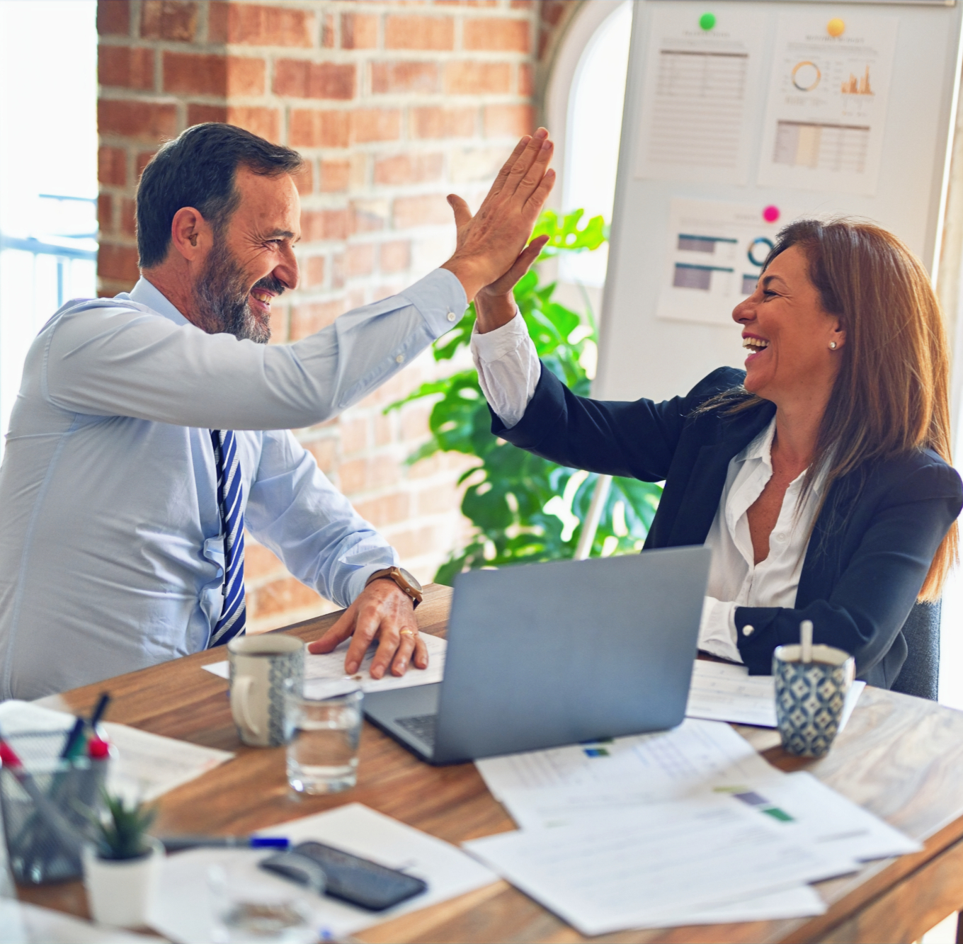 A man and woman high-fiving at a desk, celebrating a win