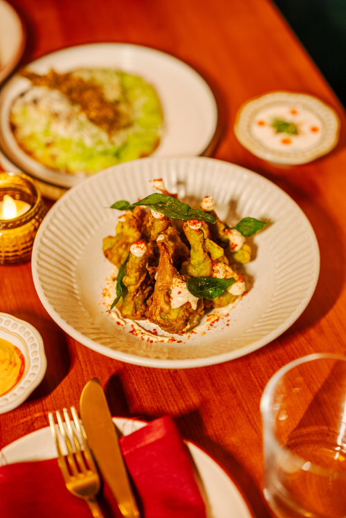 Plated Ishq dishes on a warm wood table set with gold cutlery and candlelight
