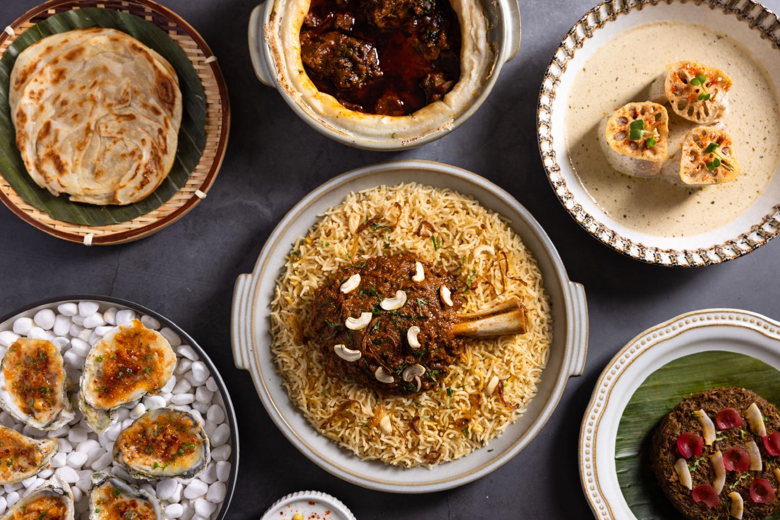 Overhead spread of Ishq dishes — flaky parathas, biryani, grilled oysters and tandoori plates on a dark table