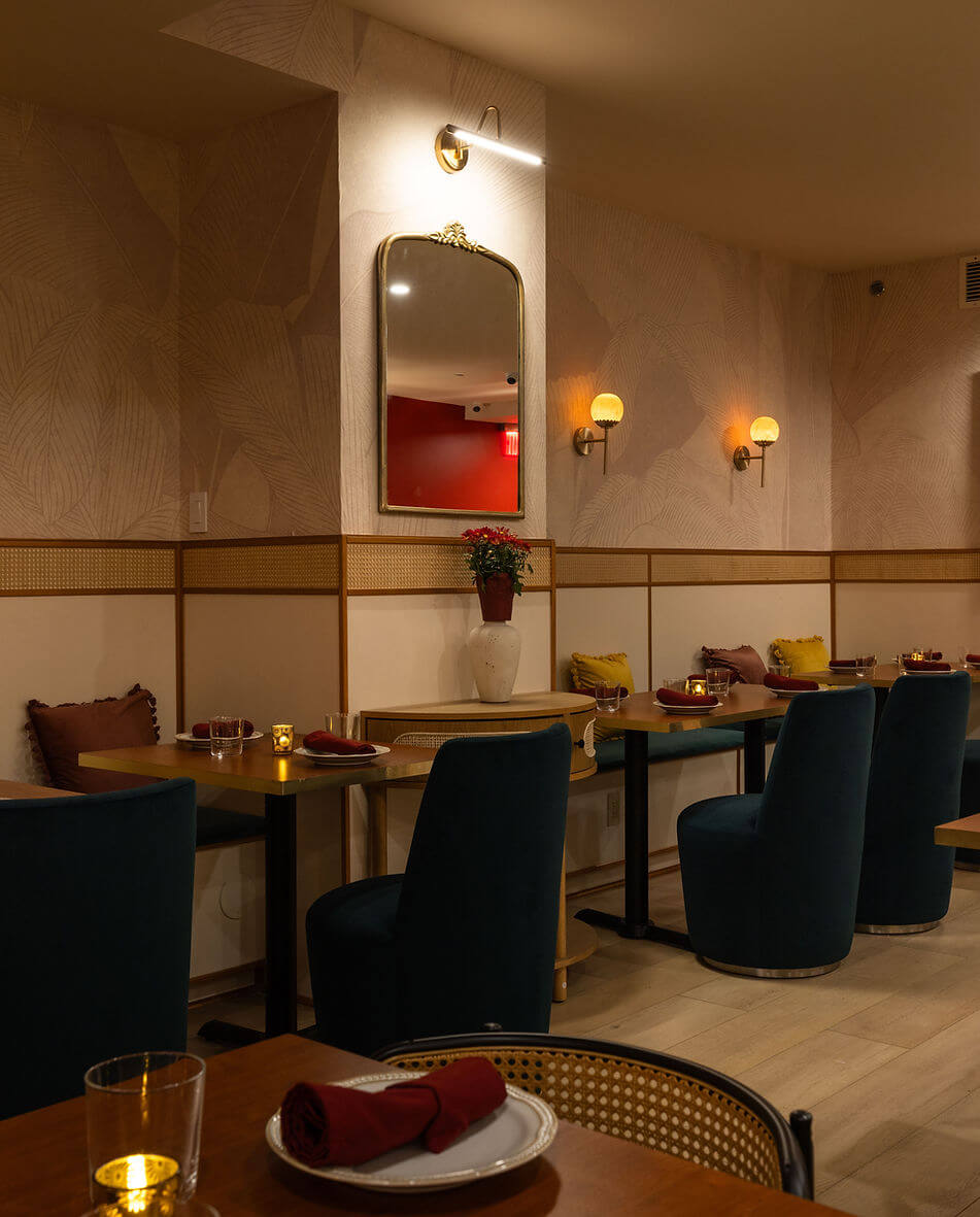 The Ishq dining room with navy chairs, brass sconces and cane detailing