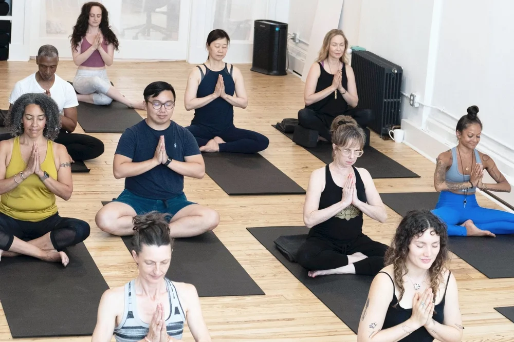 A large group of ISHTA students seated in prayer pose