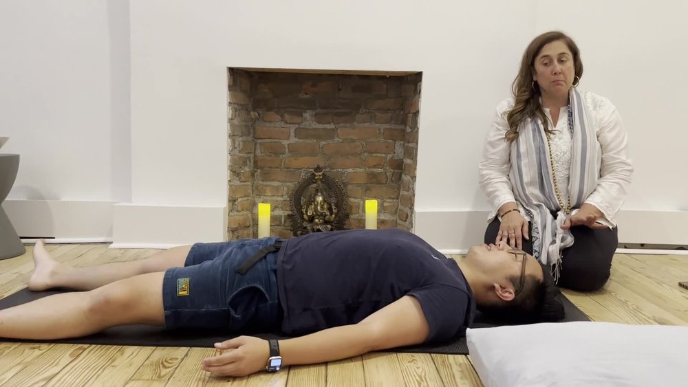 An ISHTA instructor guiding a student in savasana
