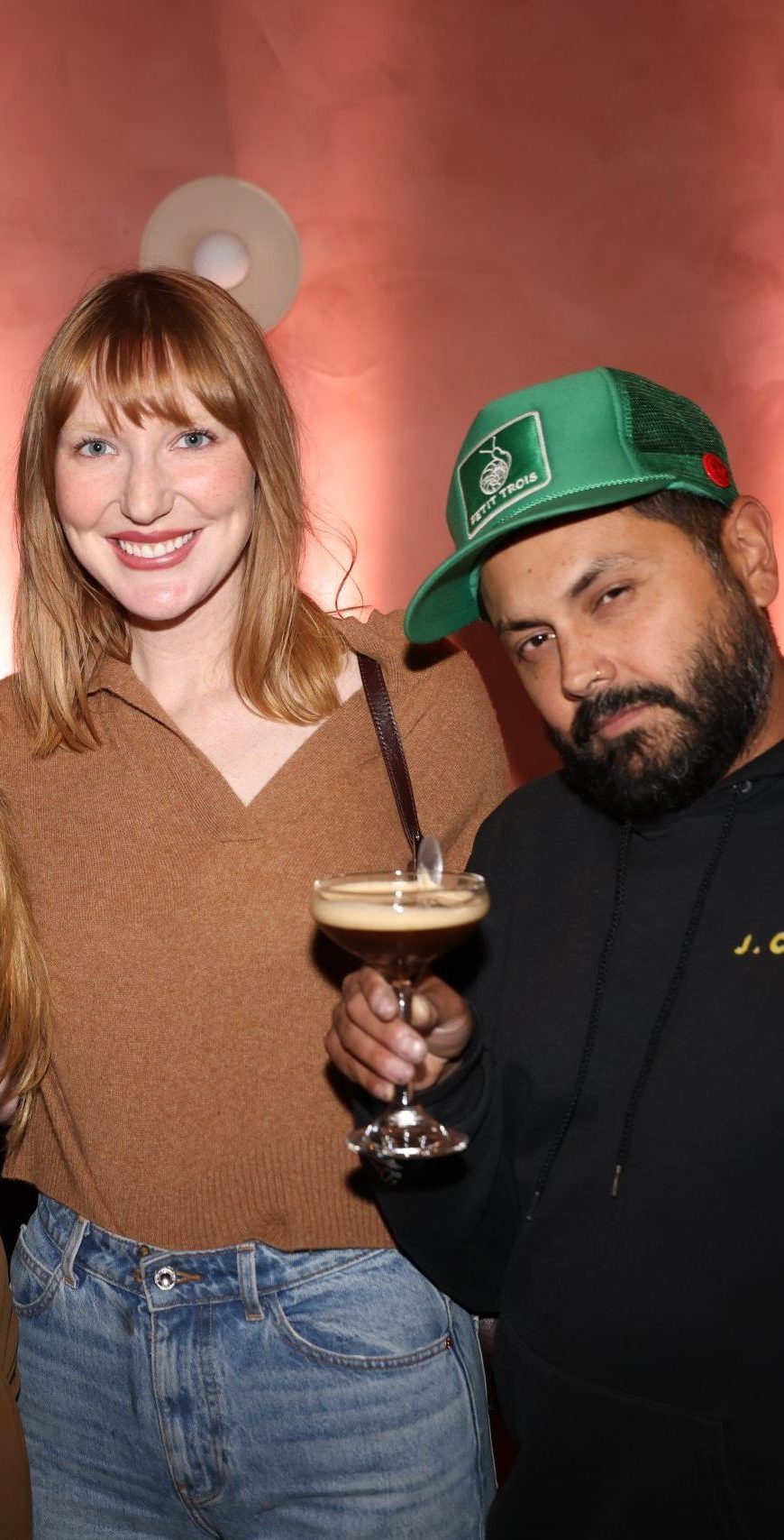 Two event guests with an espresso martini at a Petit Trois activation against a pink backdrop