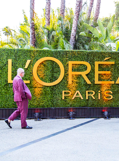 Man in pink suit walking past large L'Oréal Paris hedge wall signage