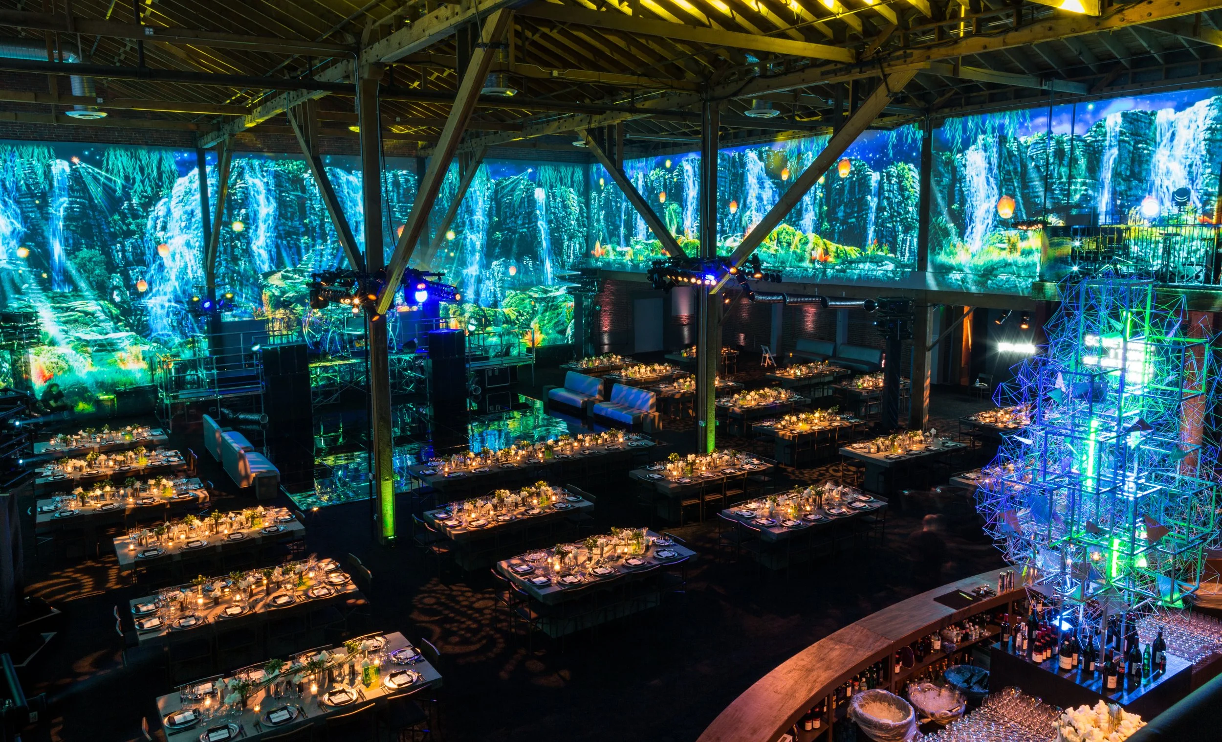 Immersive event venue with projected jungle and waterfall LED walls, set dining tables and a bar at the Berg Bar Mitzvah