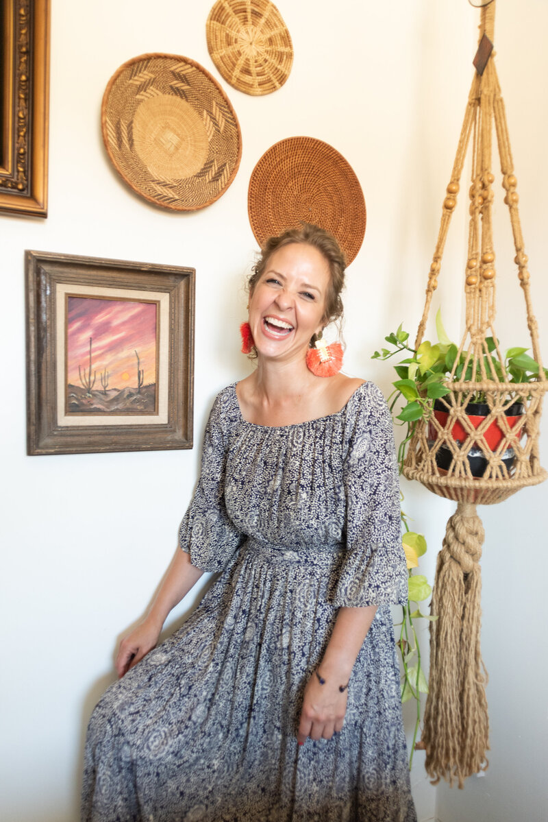 Jacqueline in a blue paisley dress laughing against a boho wall with macrame