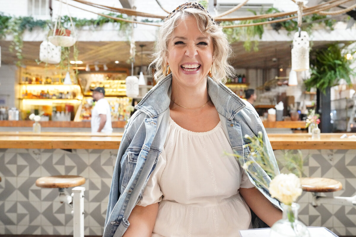 Jacqueline laughing in a leopard headband and denim jacket at a cafe bar