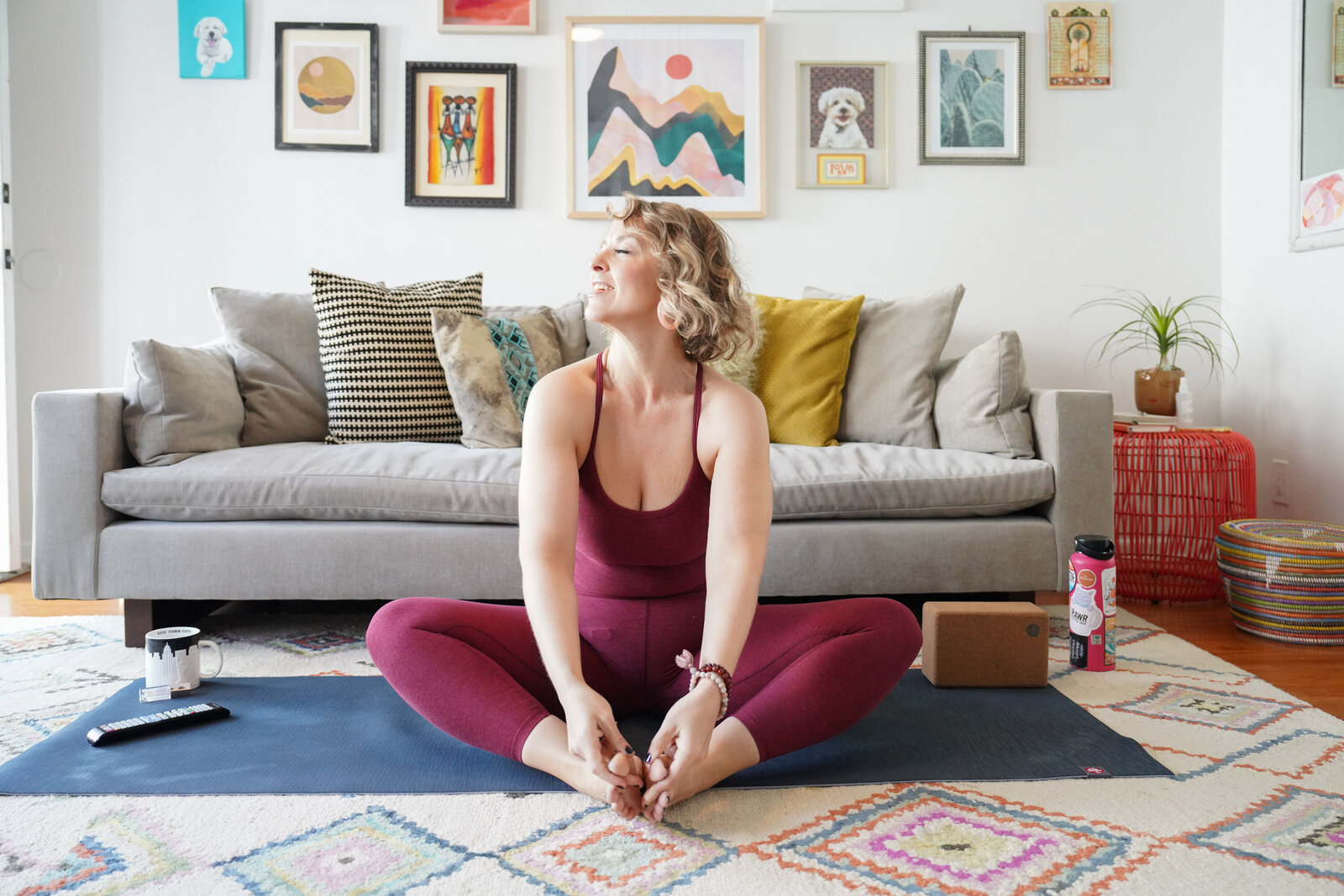Jacqueline in burgundy yoga attire, seated cross-legged on a yoga mat, eyes closed, smiling peacefully