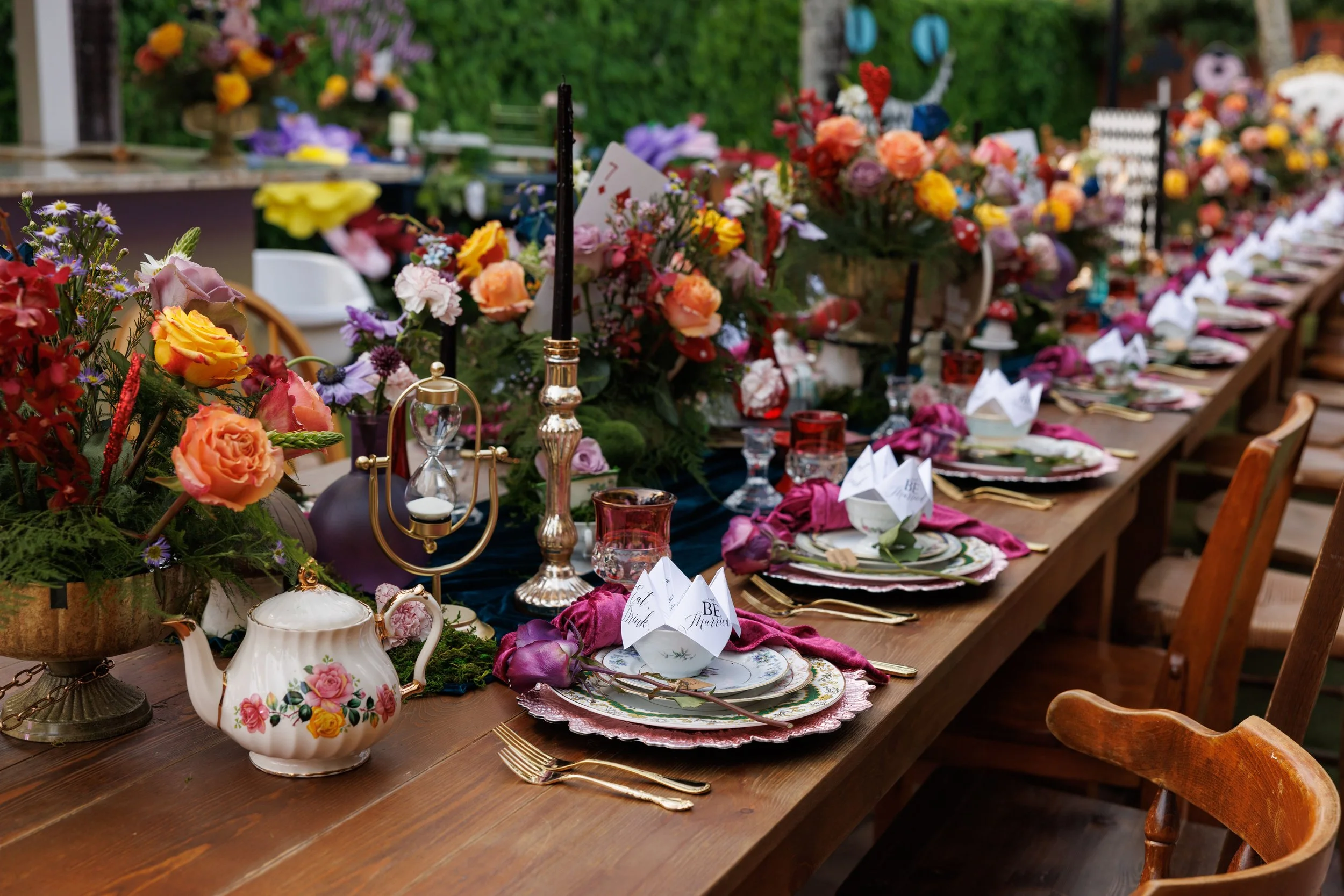 Long Alice in Wonderland dinner table with jewel-tone florals, teapots and an hourglass