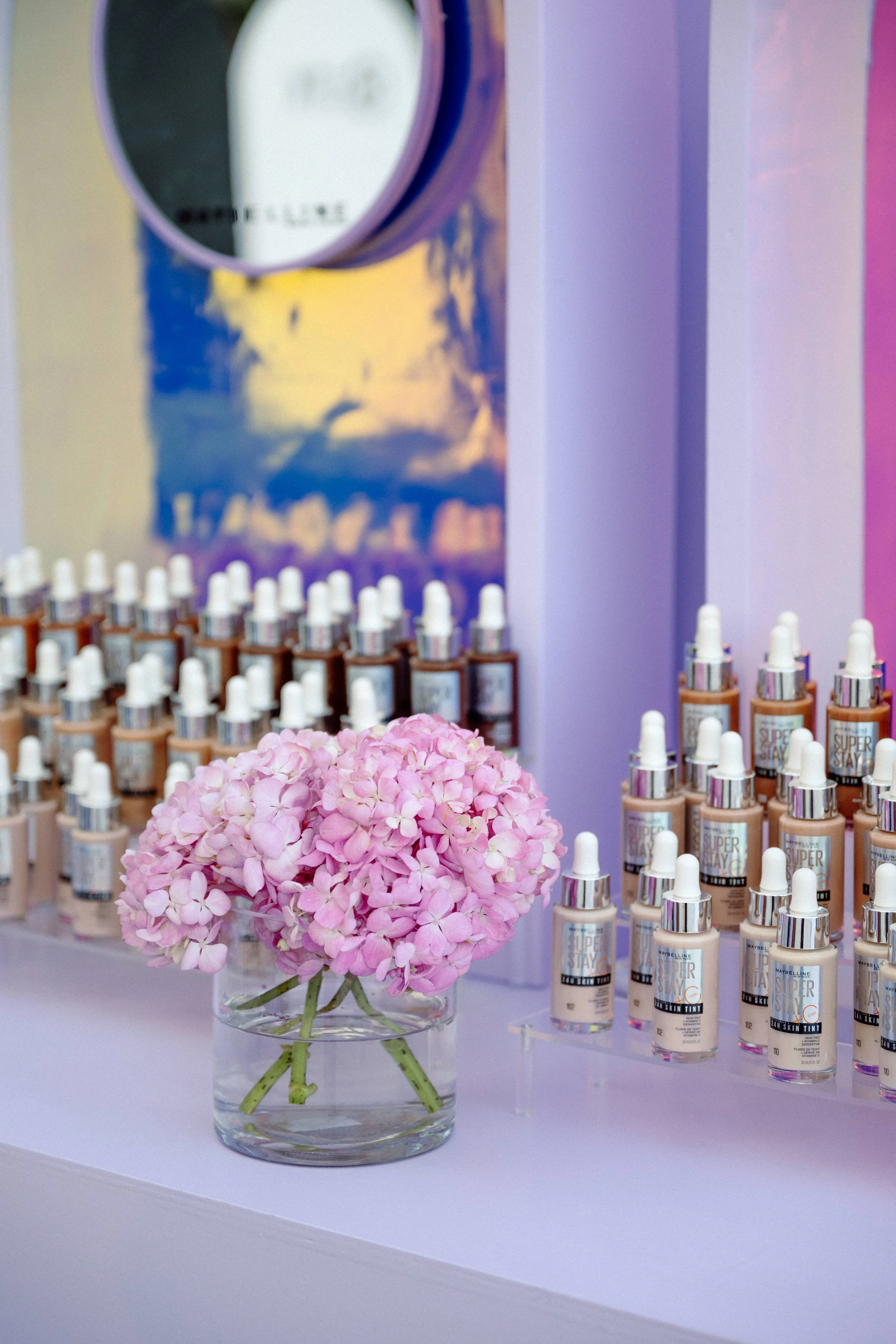 Maybelline foundation bottles displayed beside a pink hydrangea vase