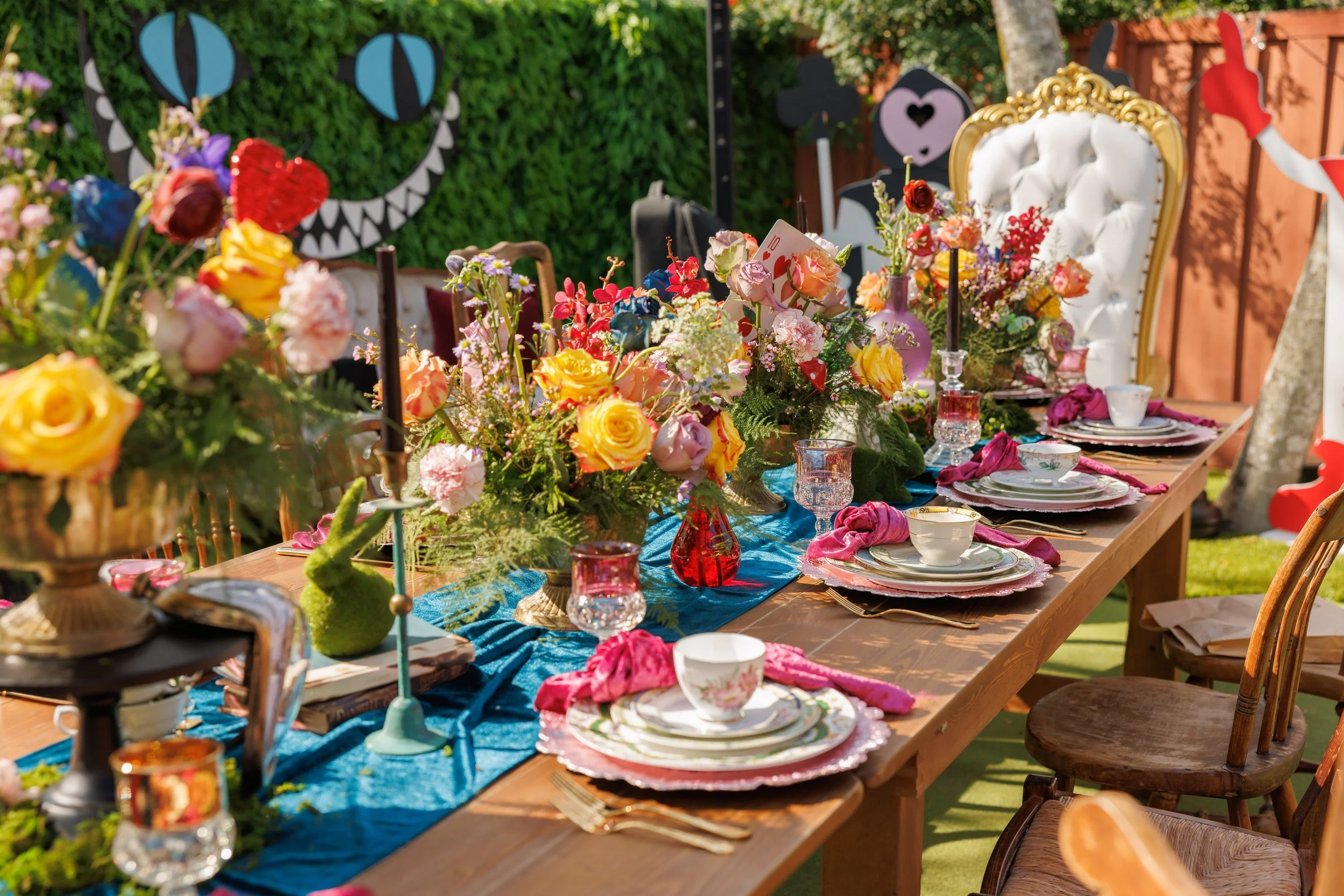 Alice in Wonderland table with a Cheshire cat backdrop, gold throne chair and colourful florals