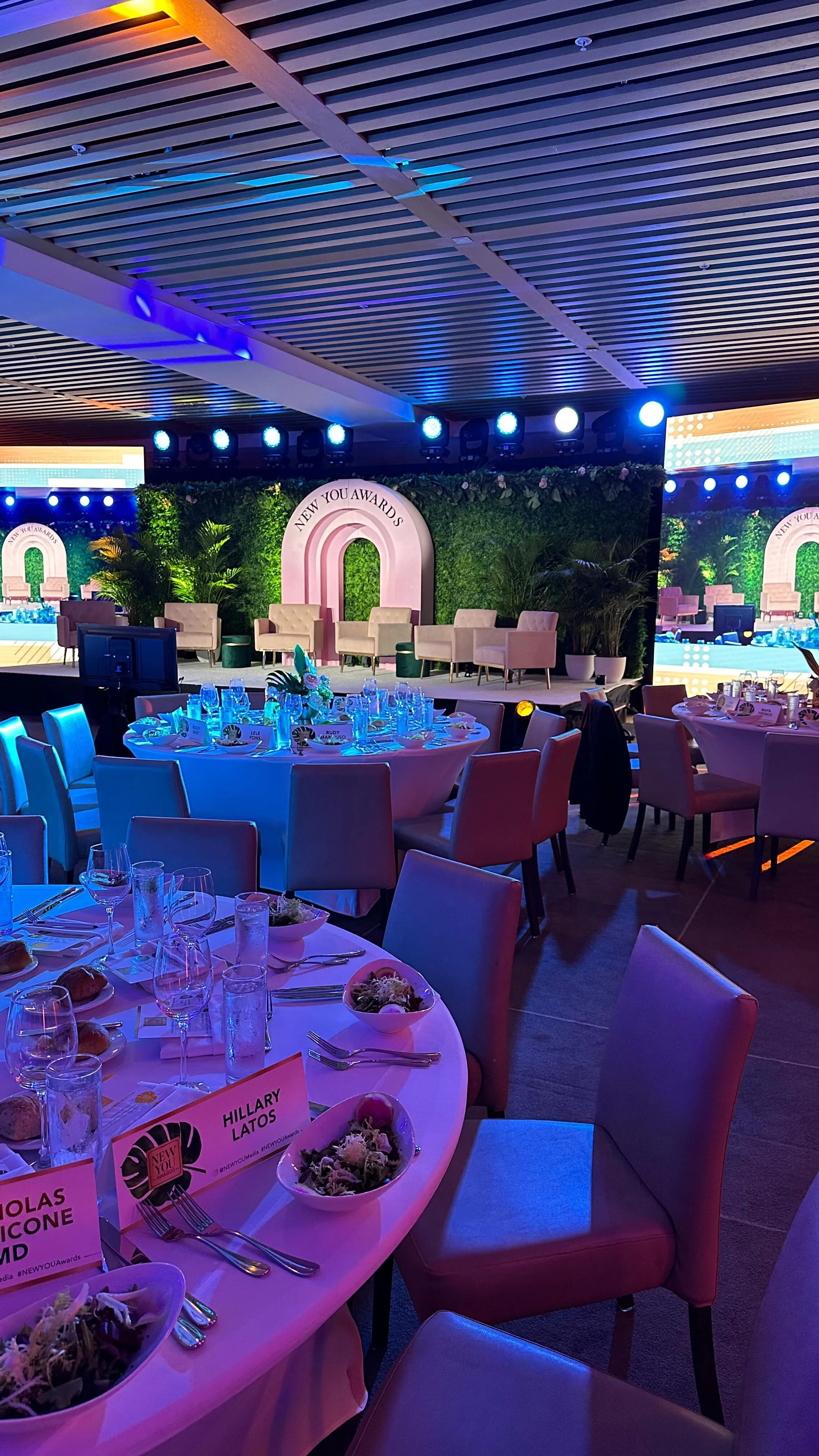 New You Awards gala with a pink arched stage backdrop, round tables and blue uplighting