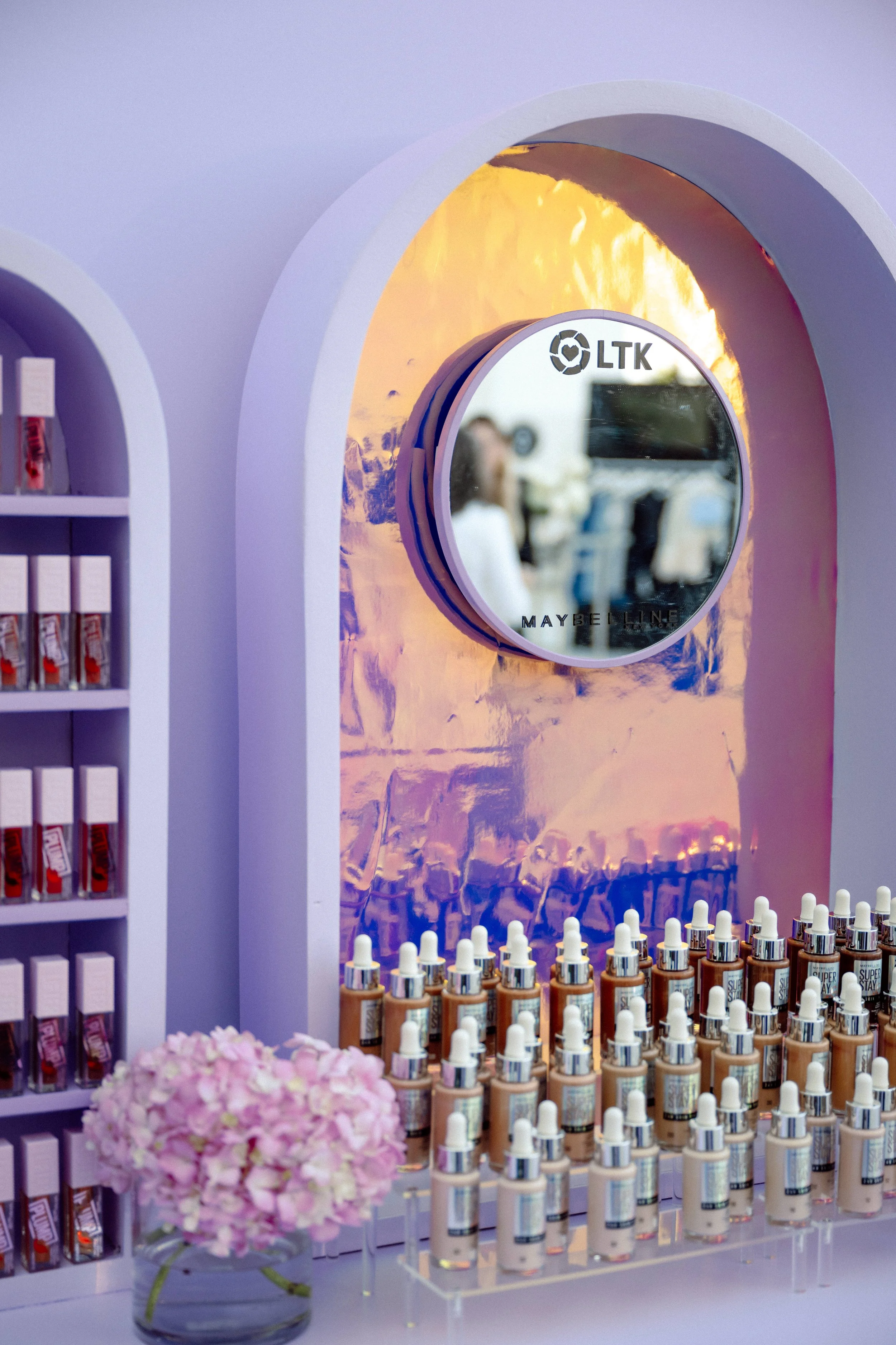 Maybelline and LTK activation booth with arched lavender display of foundation and lipstick