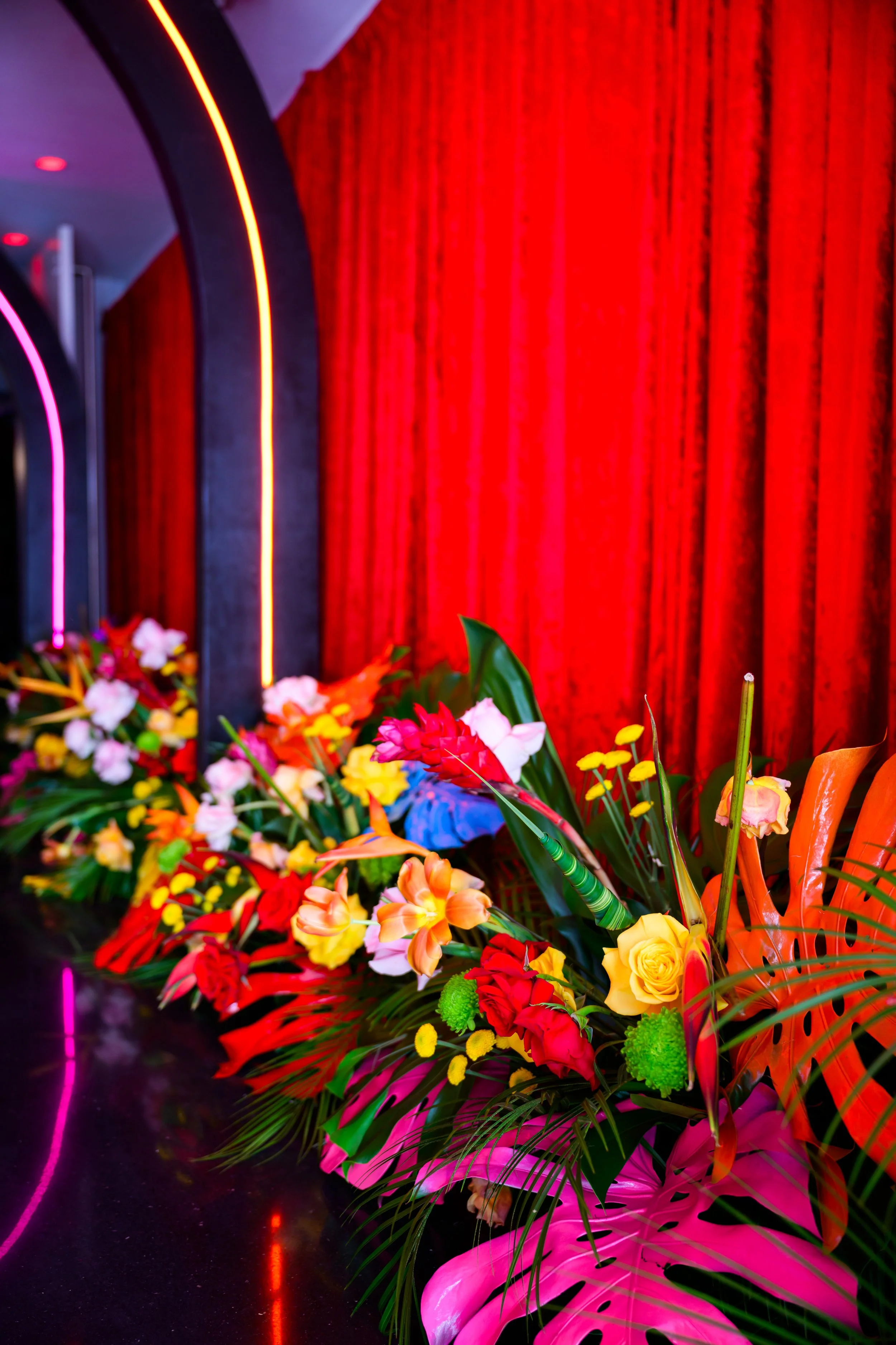 Tropical florals lining a corridor with red velvet curtain and neon arch lighting