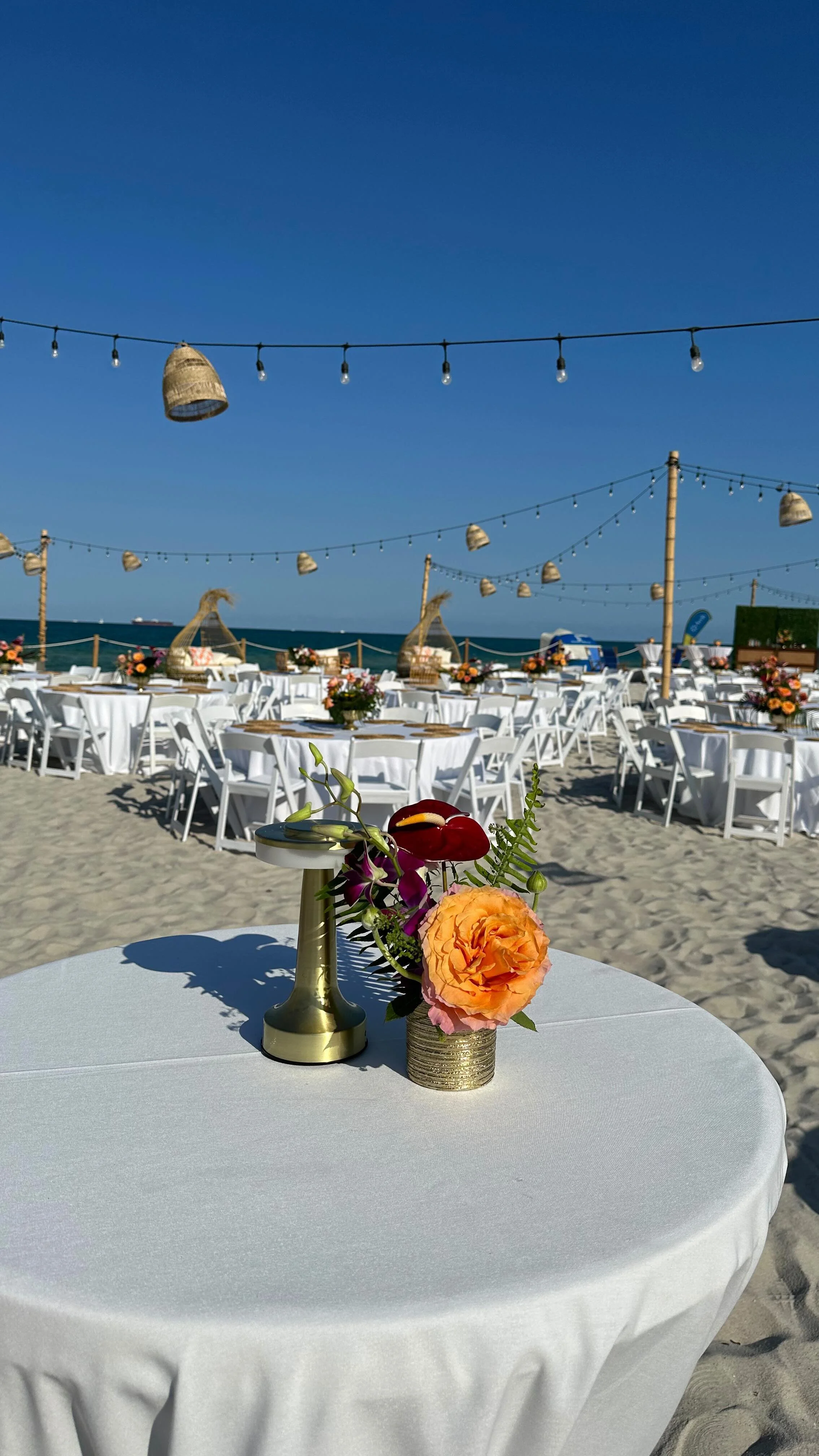Tropical beachside dinner with floral centrepieces, white linens and string lights