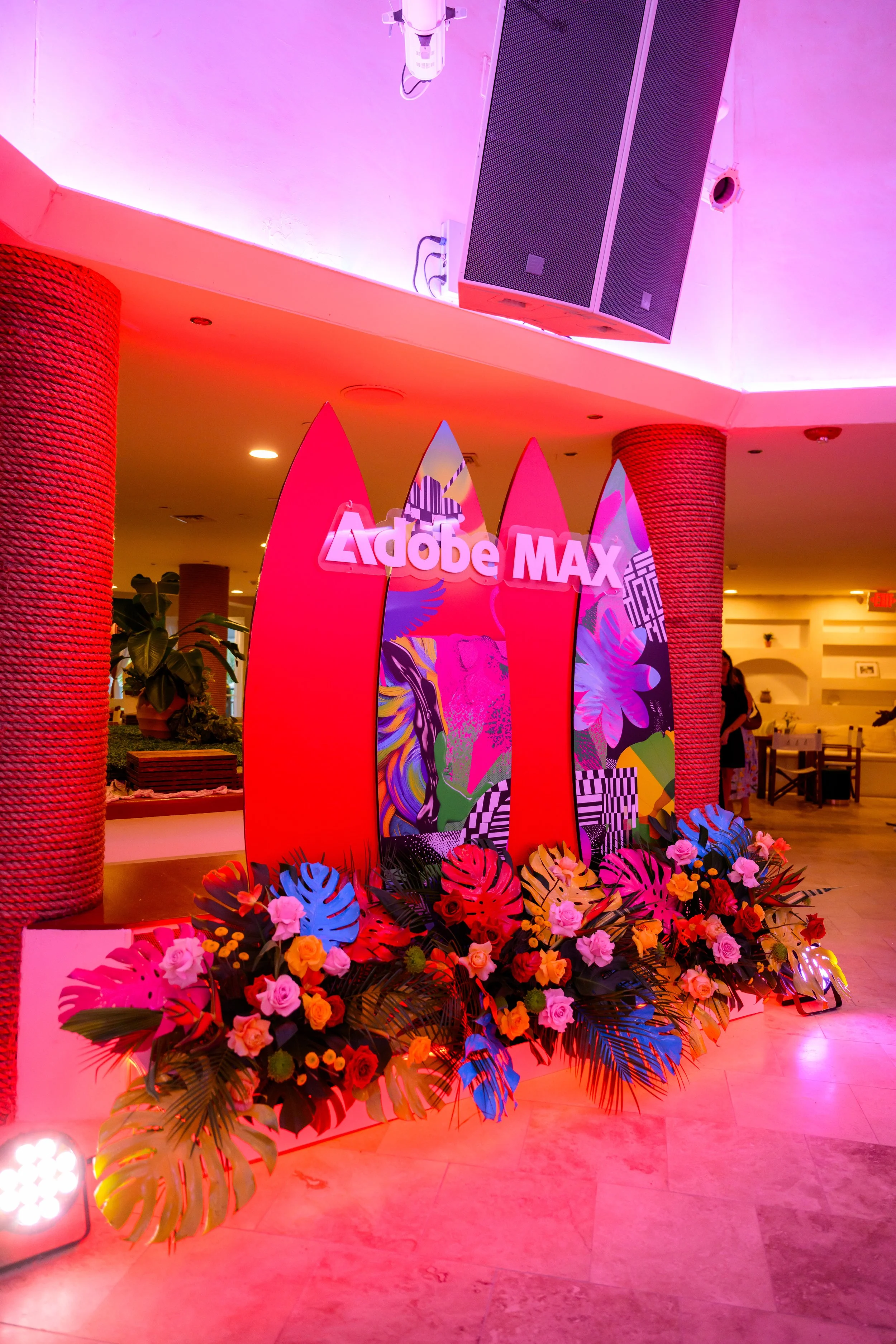 Tropical floral arrangement beside red surfboard signage under pink event lighting
