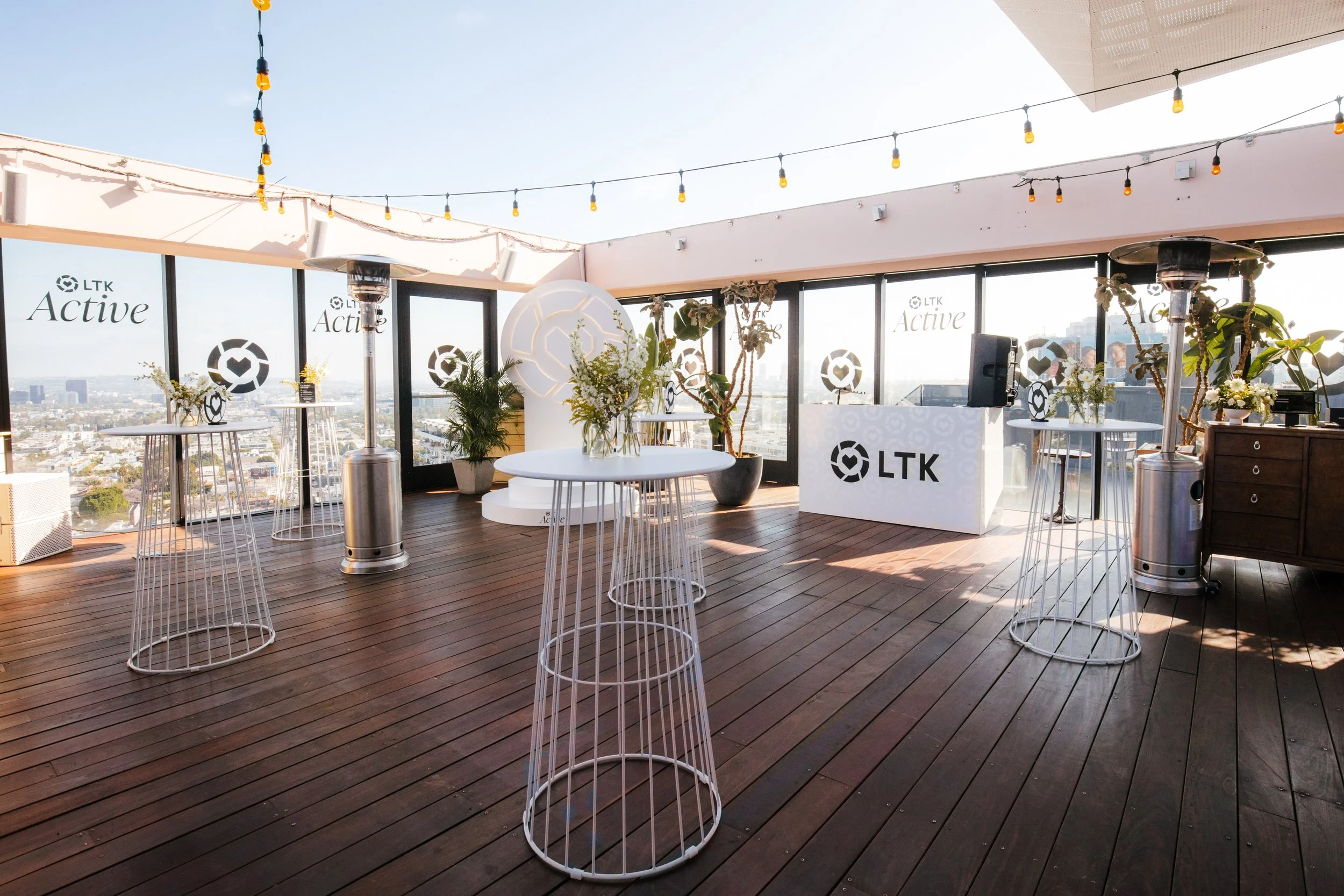 Rooftop party build with wire cocktail tables, string lights, branded DJ booth and skyline view