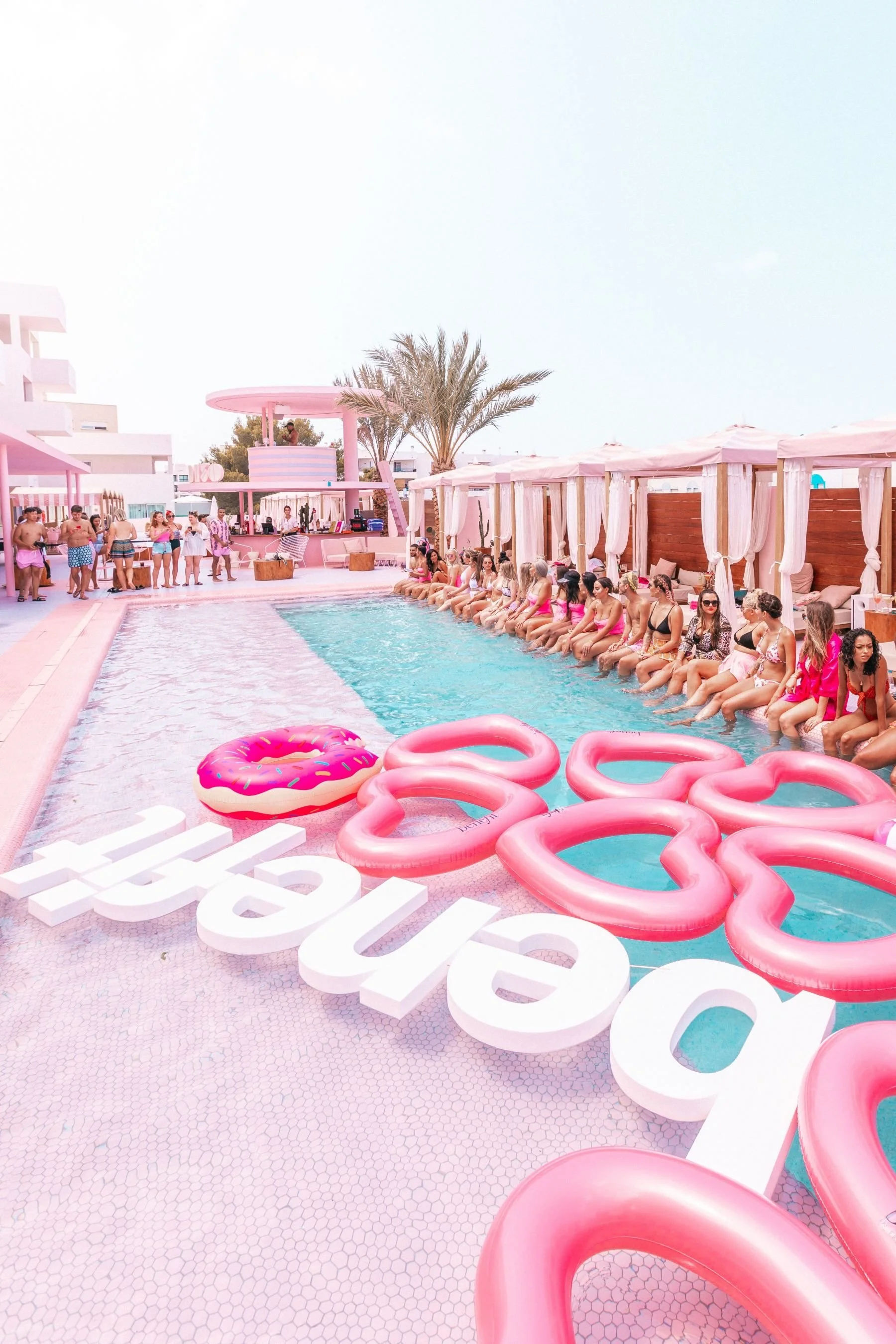 All-pink pool party with inflatable rings, floats, palms and three-dimensional beach signage
