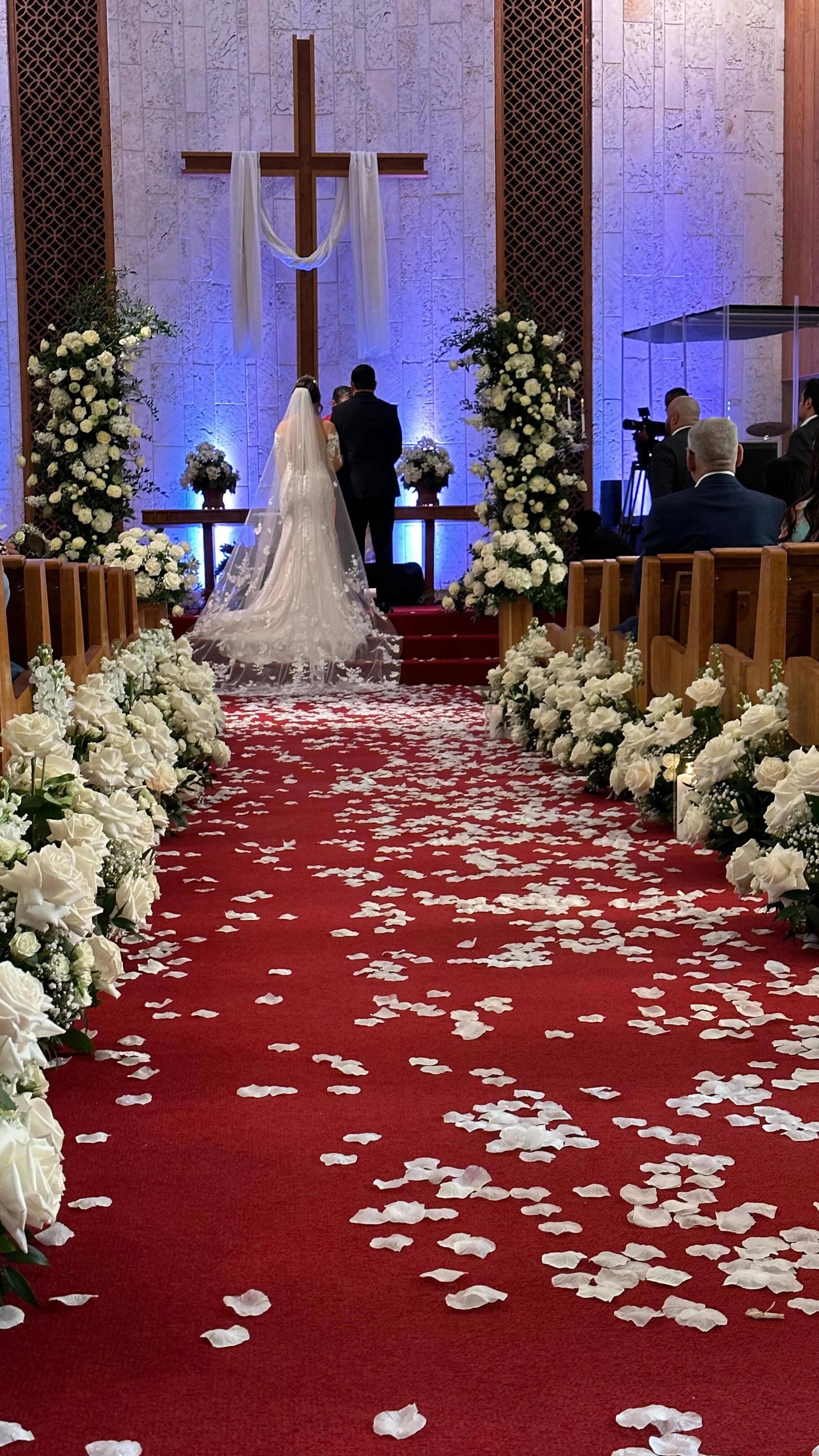 Church wedding aisle lined with white roses and petals as the bride walks toward the altar